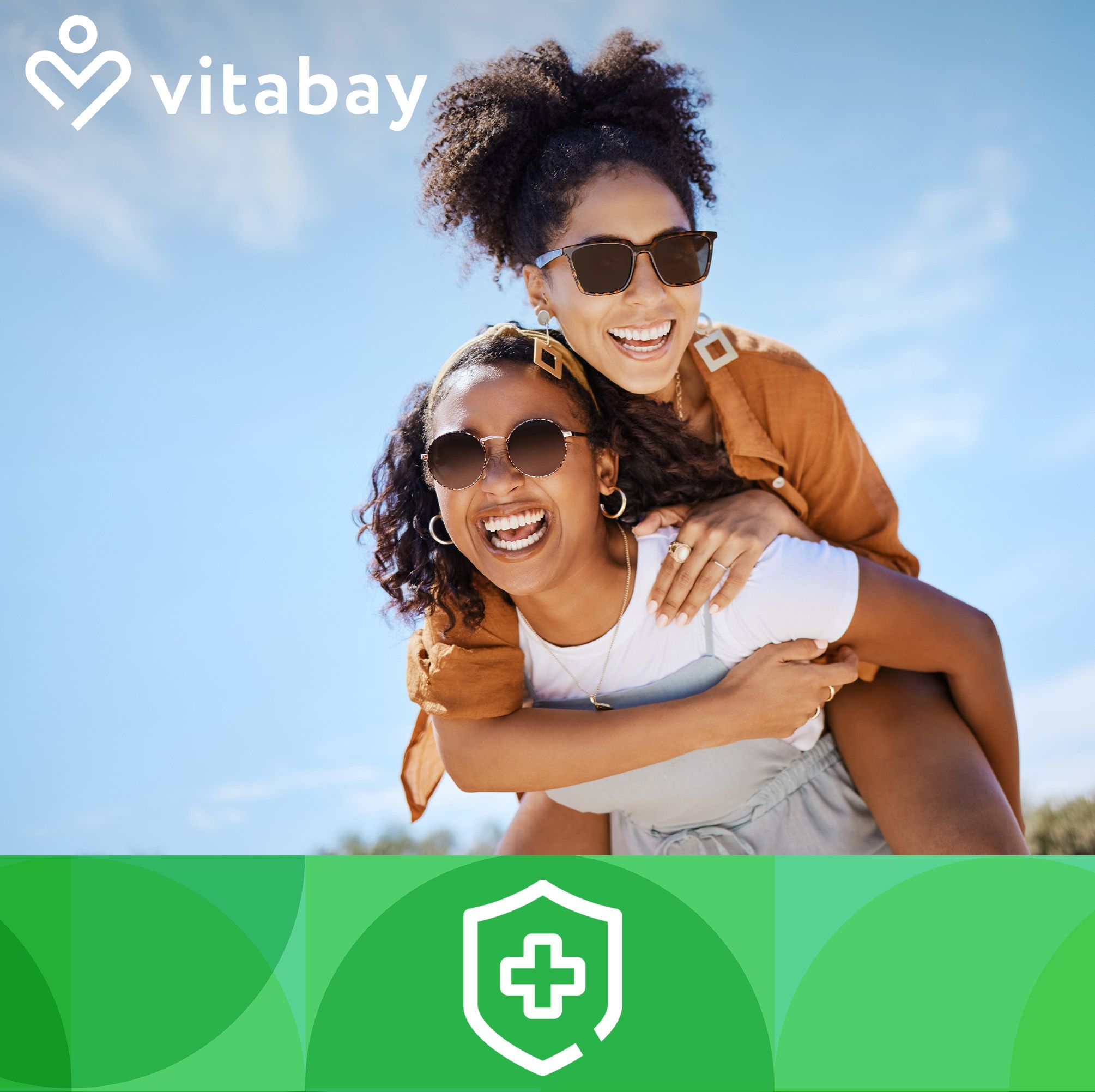 Due donne ridono all'aperto. Una porta l'altra sulle spalle. Entrambe indossano occhiali da sole. Cielo blu sullo sfondo.