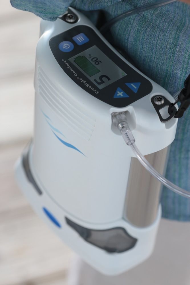 Concentratore di ossigeno portatile in uso. Dispositivo bianco con display, indossato. Logo "FreeStyle Comfort".