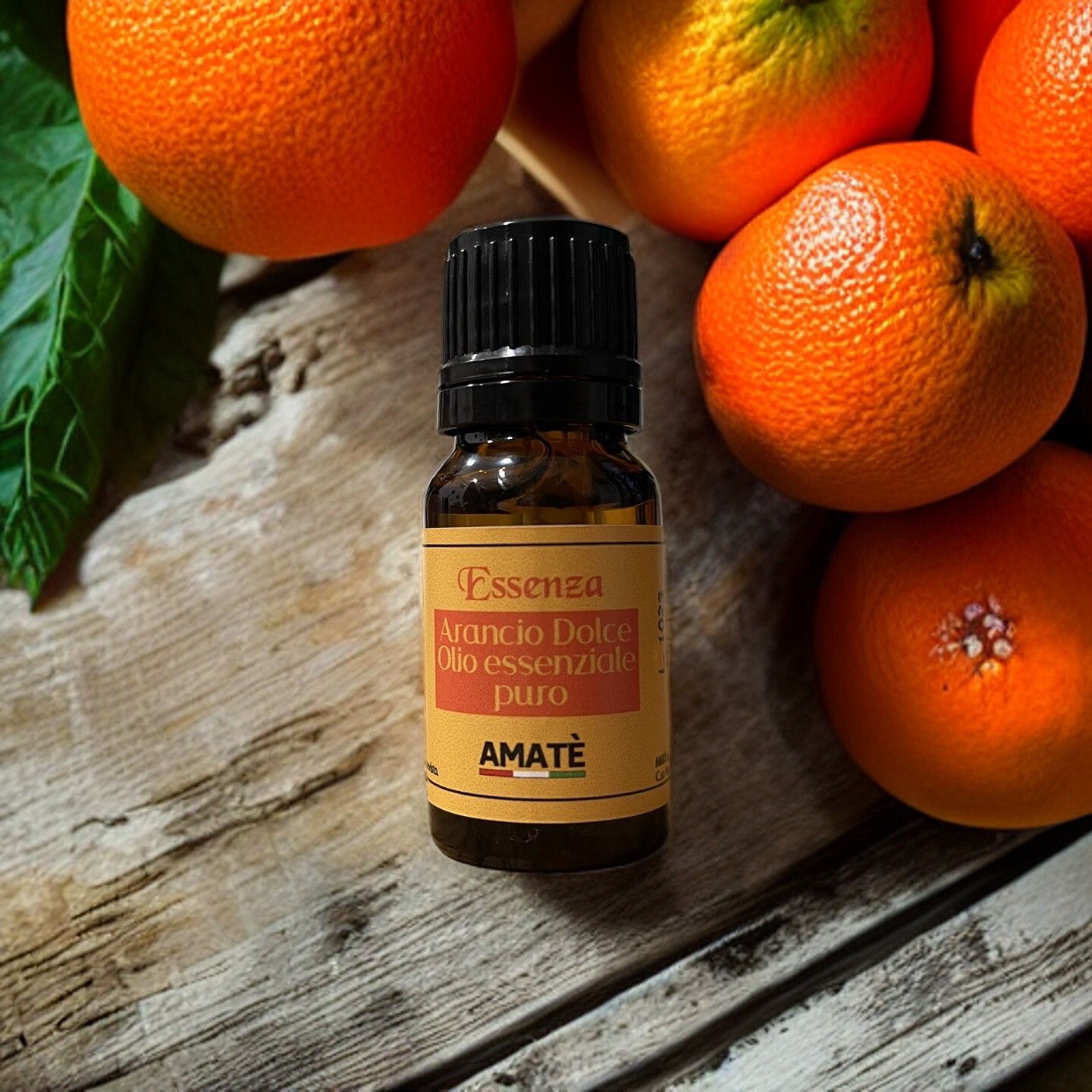 Flacone di vetro marrone con tappo nero, circondato da arance. Etichetta con testo: Arancio Dolce, Olio essenziale puro, AMATÈ.