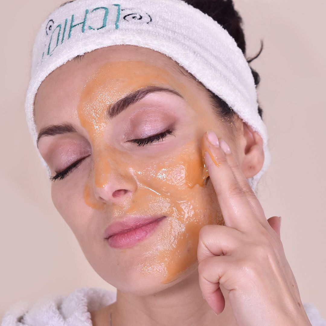 Donna con occhi chiusi, viso coperto da maschera giallastra. Fascia con logo.