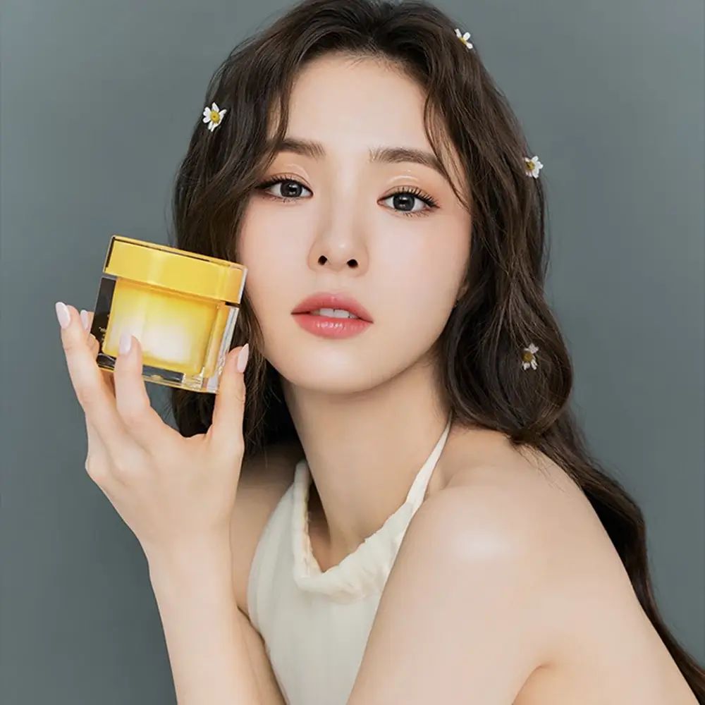 Donna tiene un barattolo di crema giallo trasparente. Prodotto per la cura del viso. Coperchio giallo, barattolo trasparente. Donna con fiori.