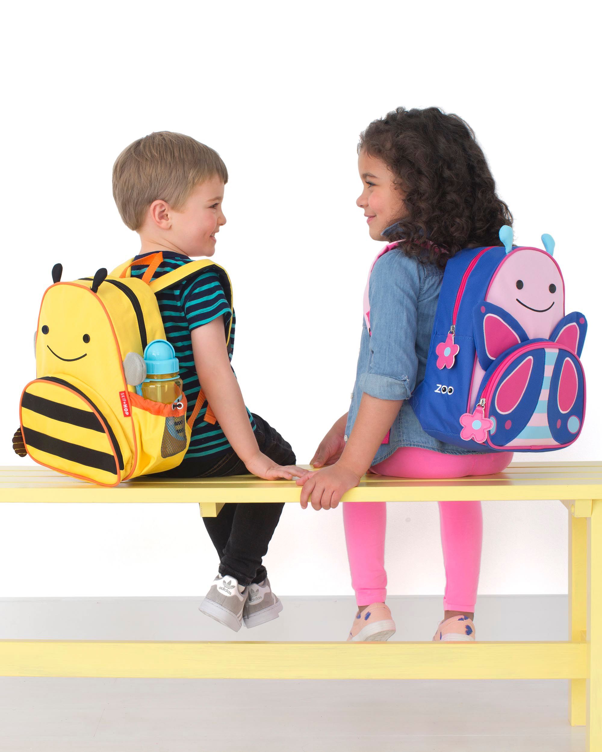Un ragazzo e una ragazza seduti uno di fronte all'altra. Il ragazzo ha uno zaino a forma di ape gialla, la ragazza uno zaino a farfalla.