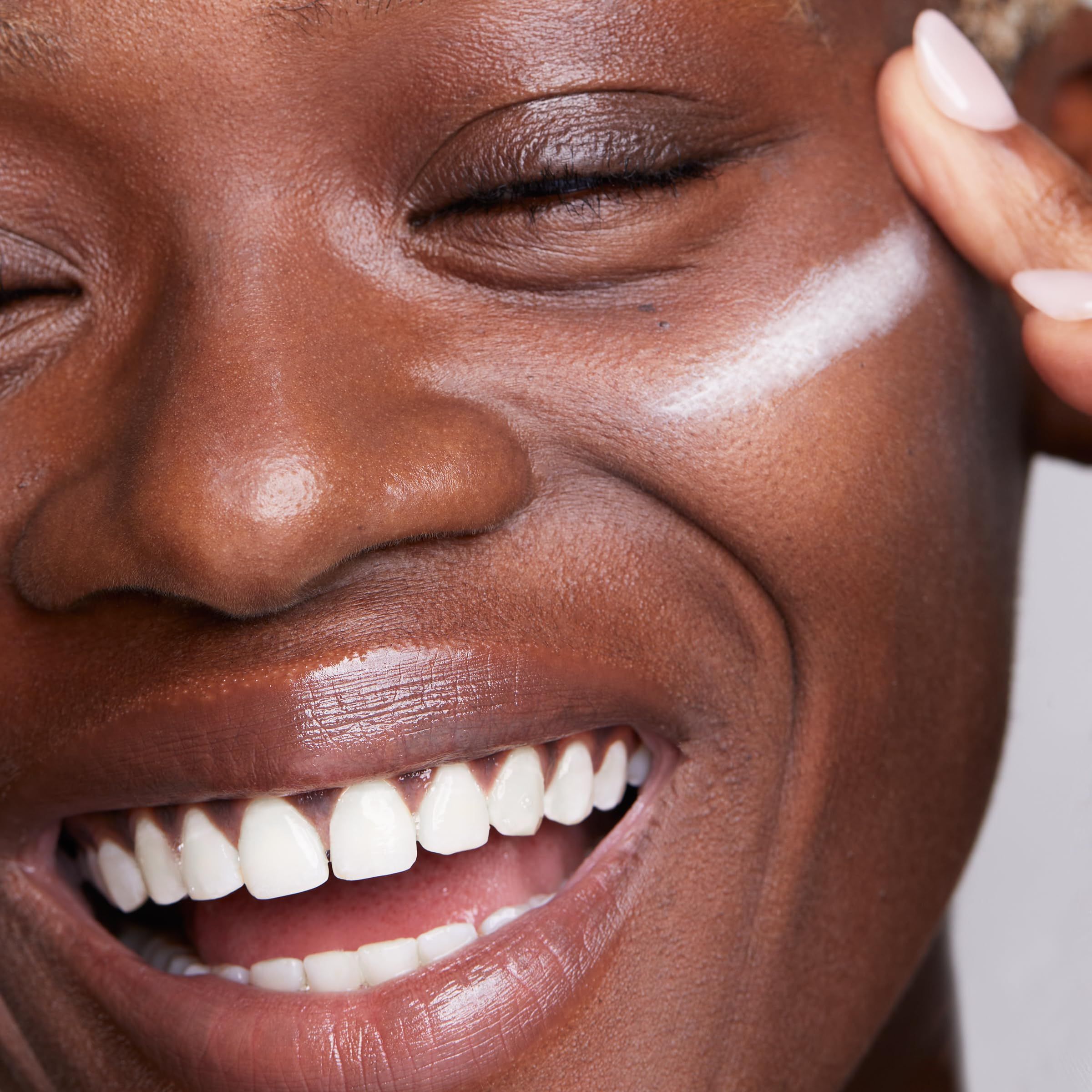 Primo piano di un viso sorridente. Prodotto applicato sulla guancia.