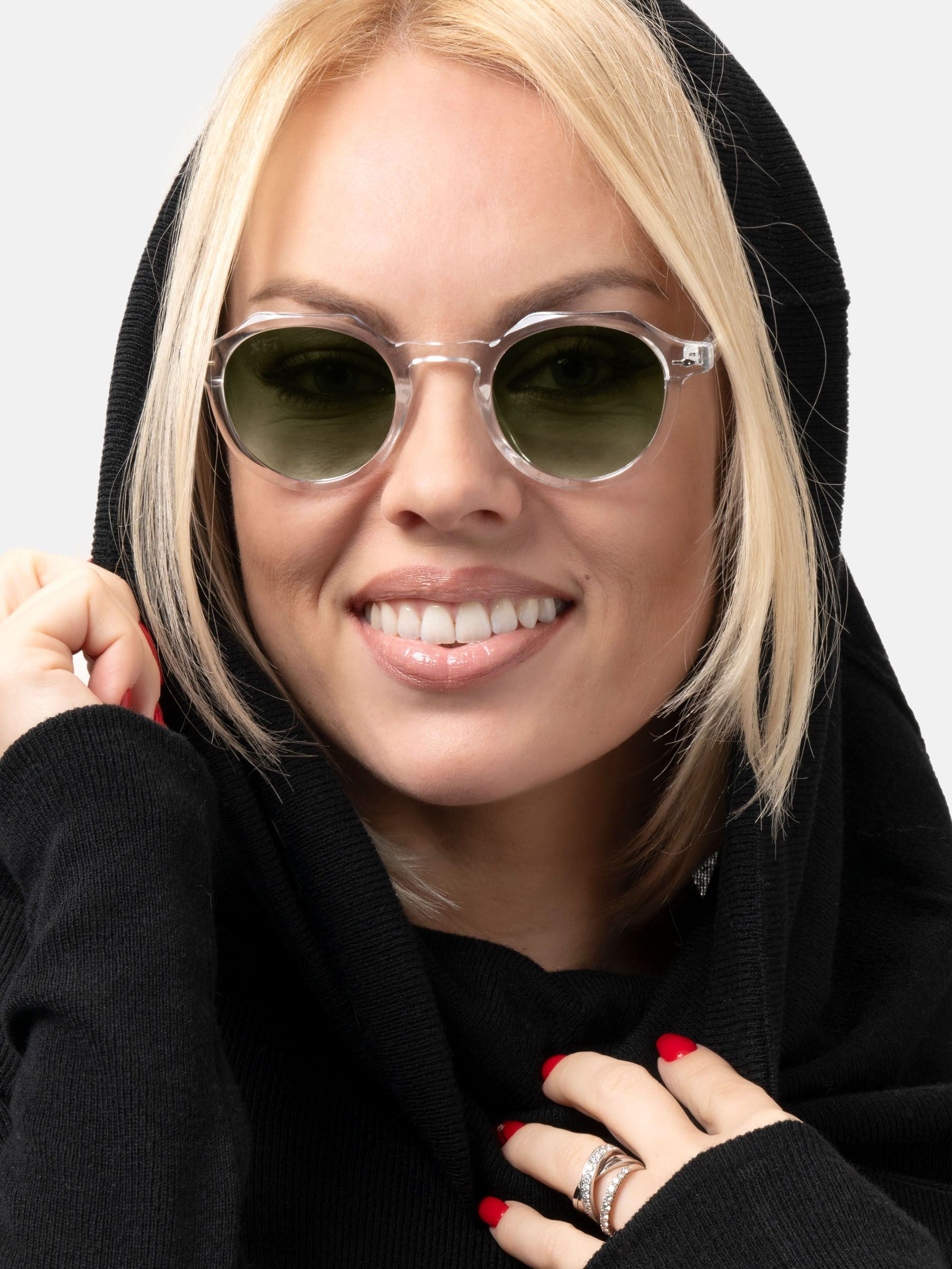 Donna bionda con occhiali da sole con montatura trasparente e lenti verdi. Sorride.