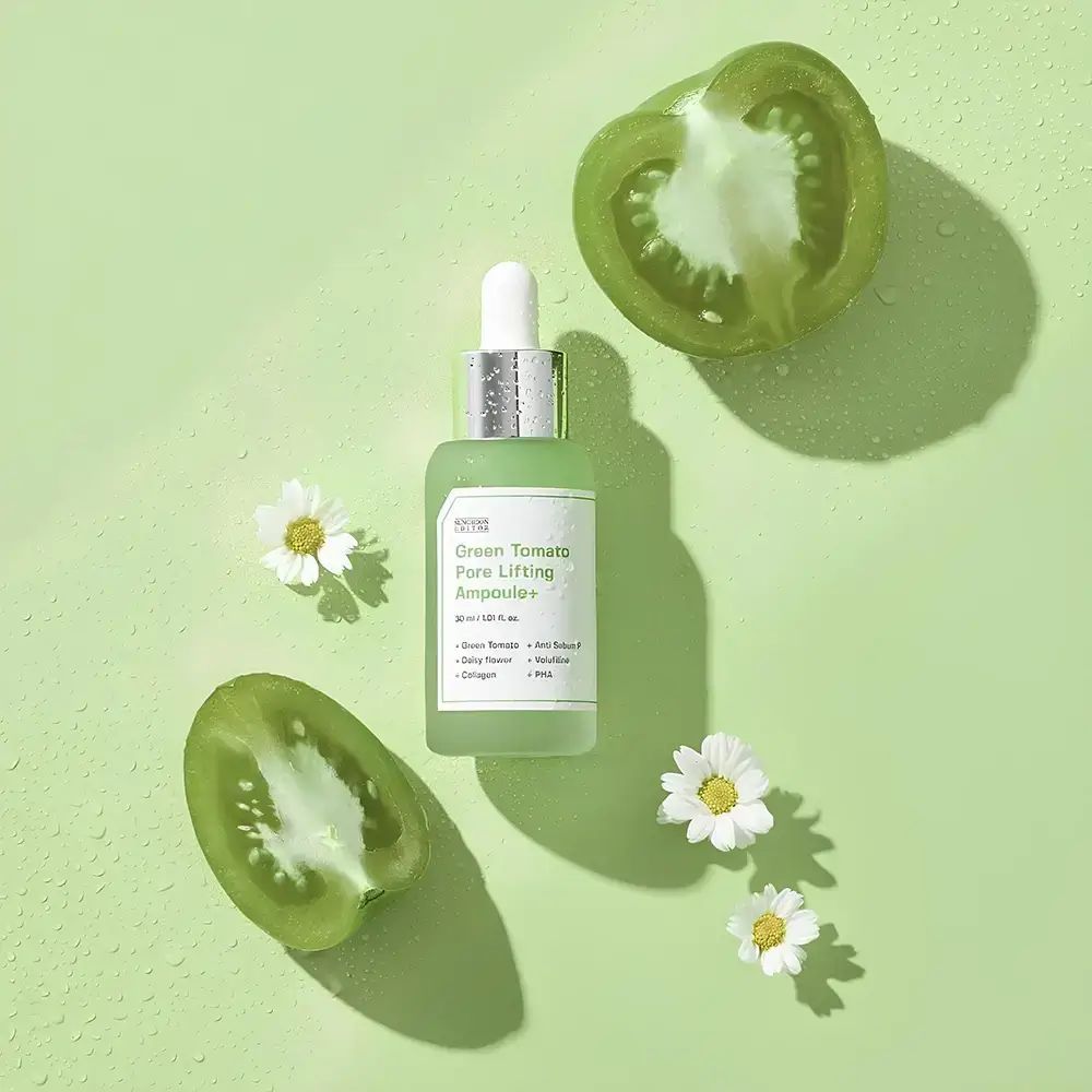 Flacone di siero verde, metà di pomodori verdi e margherite su sfondo verde.