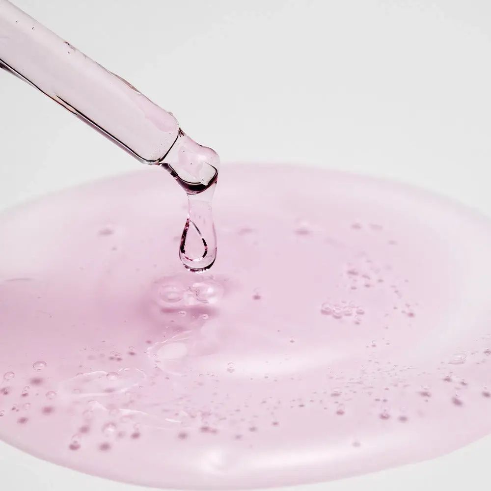 Contagocce con liquido rosa che gocciola in una pozza. Liquido con bolle. Sfondo bianco.