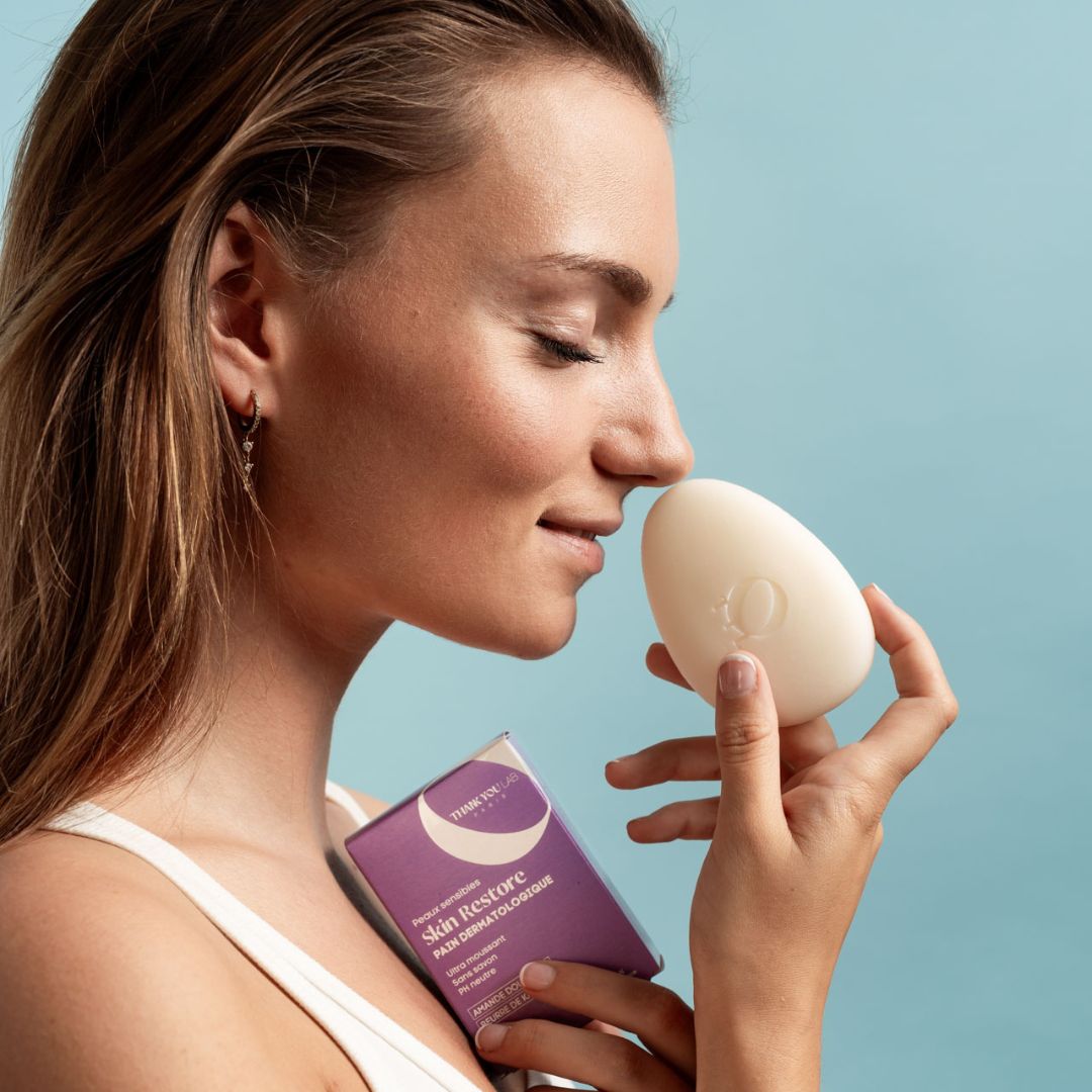 Una donna tiene una saponetta ovale e una scatola viola. Sta annusando il sapone.