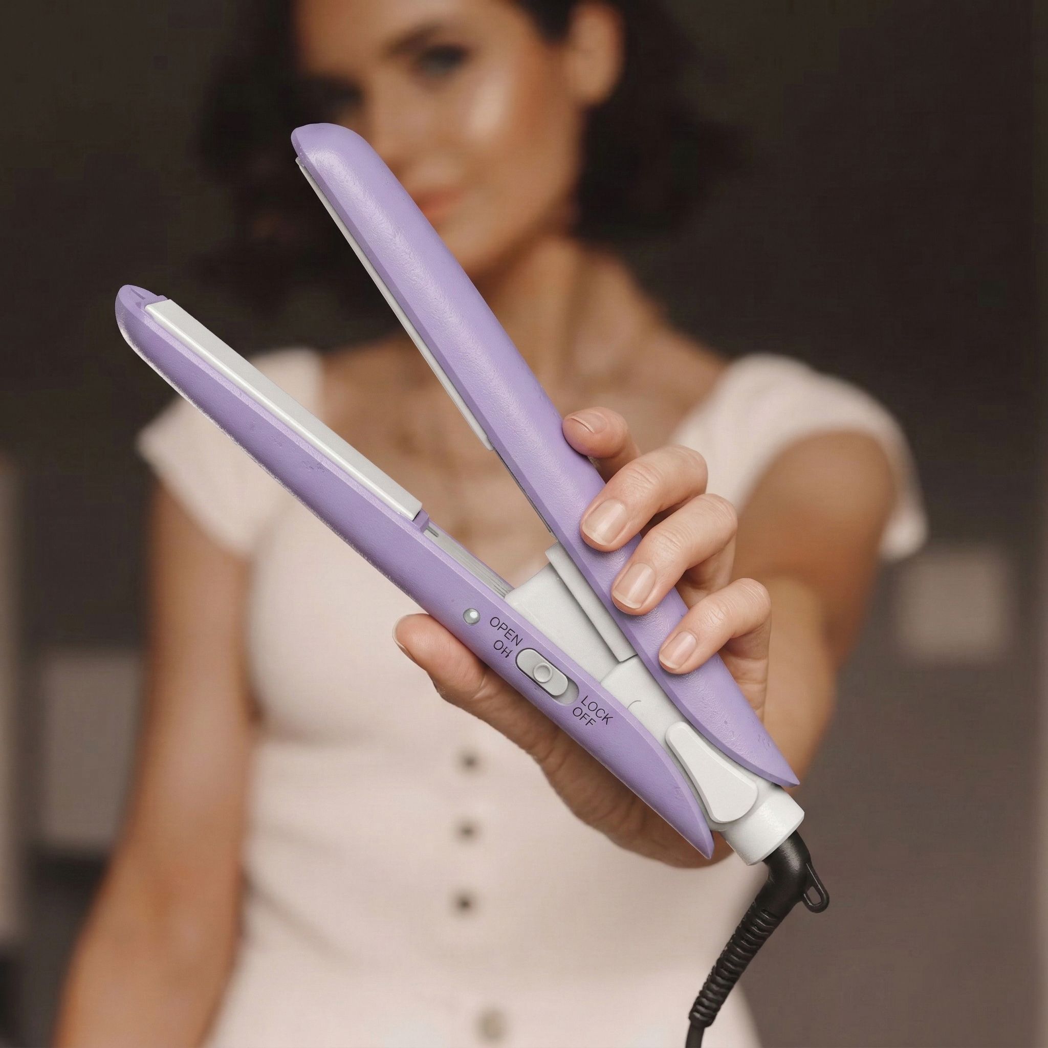 Una donna tiene una piastra per capelli viola con cavo bianco e controlli visibili.