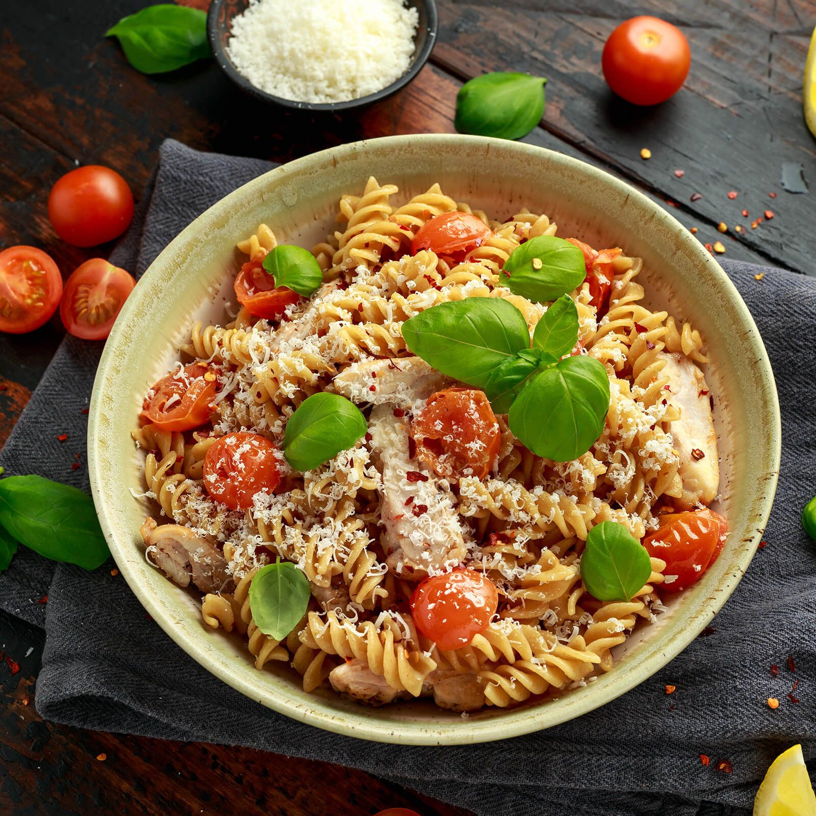 Ciotola con fusilli, pomodori, basilico, pollo e formaggio. Su tavolo di legno scuro.