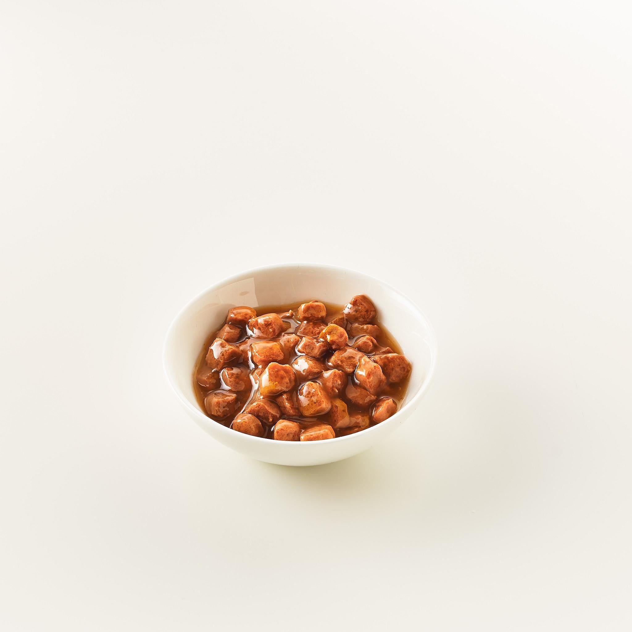 Piccoli pezzi rotondi in una ciotola bianca. I pezzi sono in una salsa marrone.