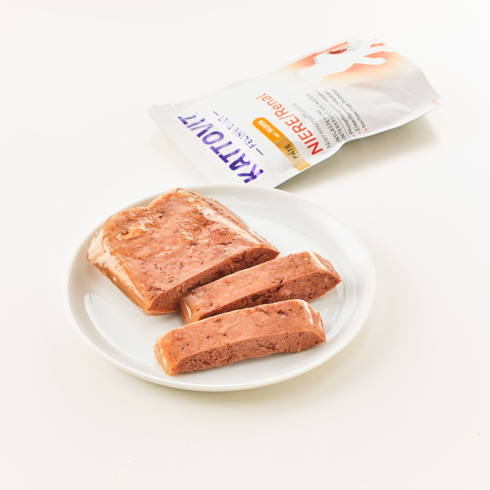 Pâté per gatti tagliato su un piatto bianco. Accanto, una confezione aperta con logo KATTOVIT e testo "Niere/Renal".