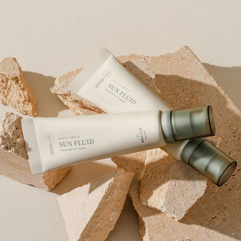 Due tubi 'DAILY MILD SUN FLUID' su pietre. Tappi verdi, colore chiaro.