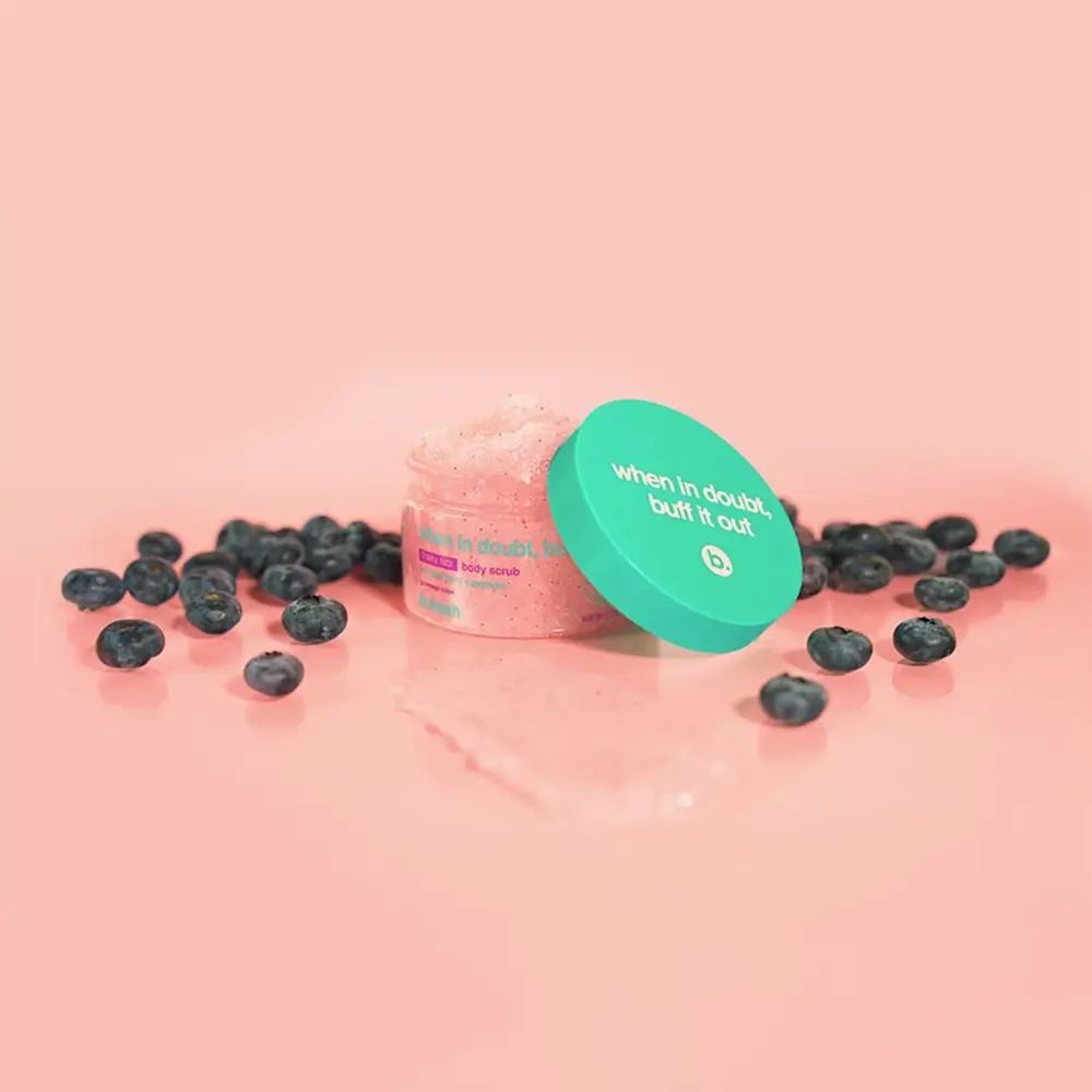 Vaso di scrub aperto, coperchio blu, mirtilli. Testo sul coperchio: When in doubt, buff it out. Contenuto rosa visibile.