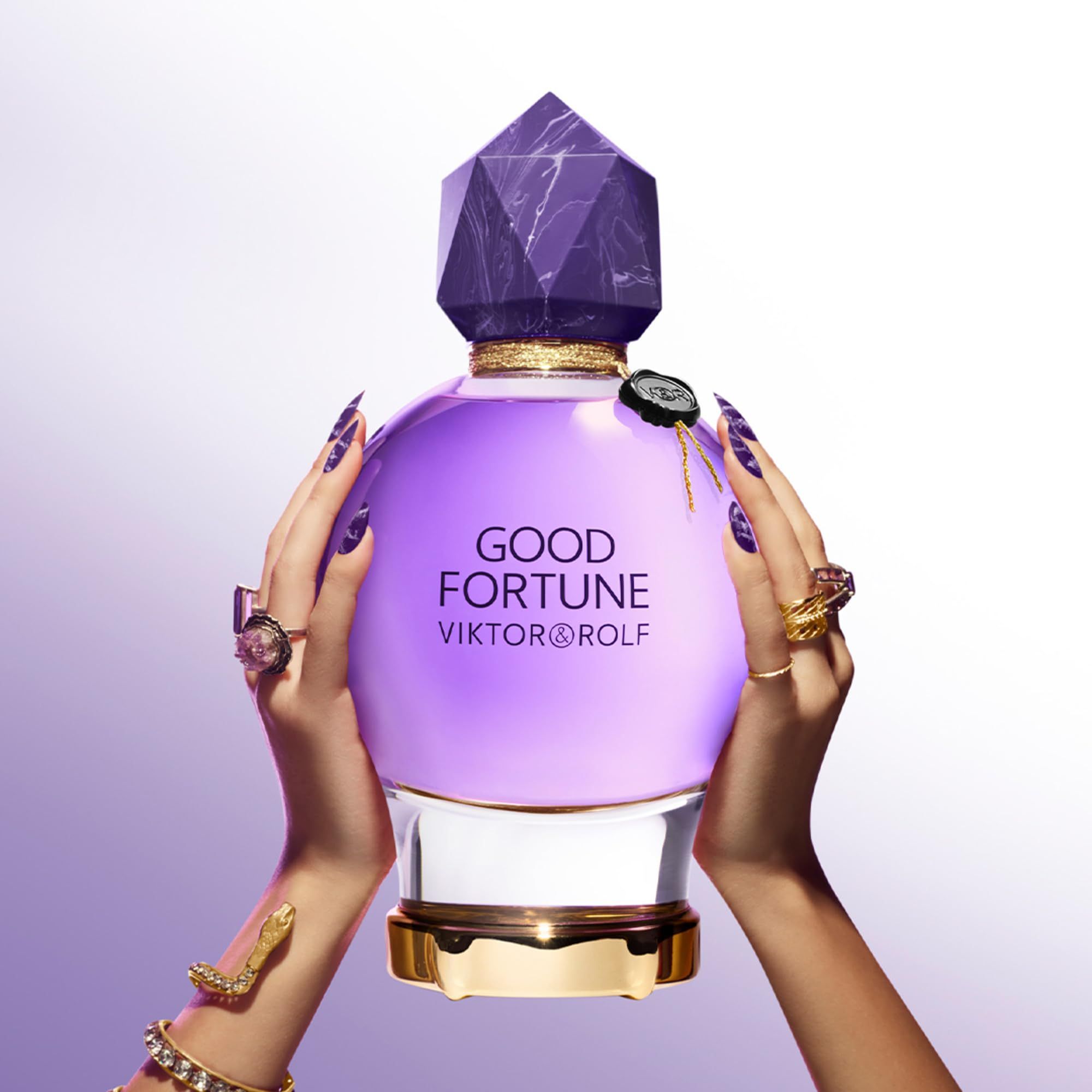 Flacone viola con tappo di cristallo, tenuto da mani con unghie e anelli. Scritta: Good Fortune, Viktor & Rolf.