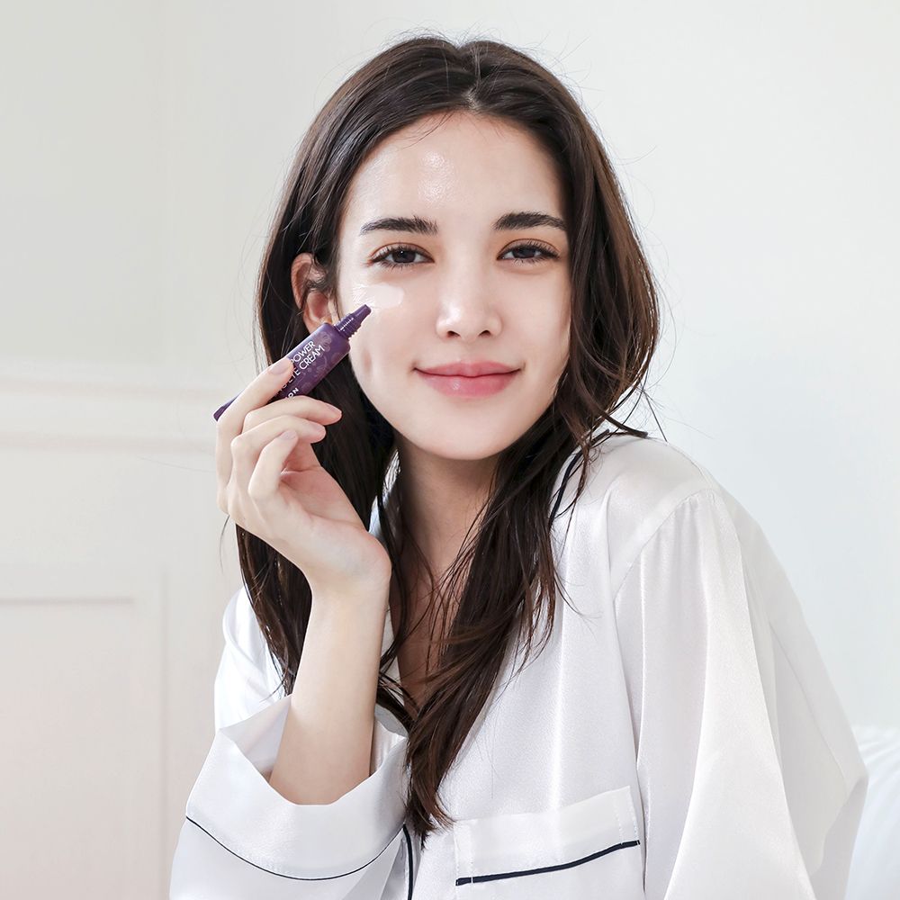 Donna che tiene in mano un tubo MIZON Collagen Power Firming Eye Cream. Tubo viola, tappo rosa. Testo: Collagen Power Firming Eye Cream.