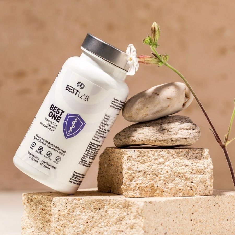 Flacone bianco BEST LAB BEST ONE, accanto a pietre e pianta. Contiene vitamine D, K, magnesio. 60 capsule.