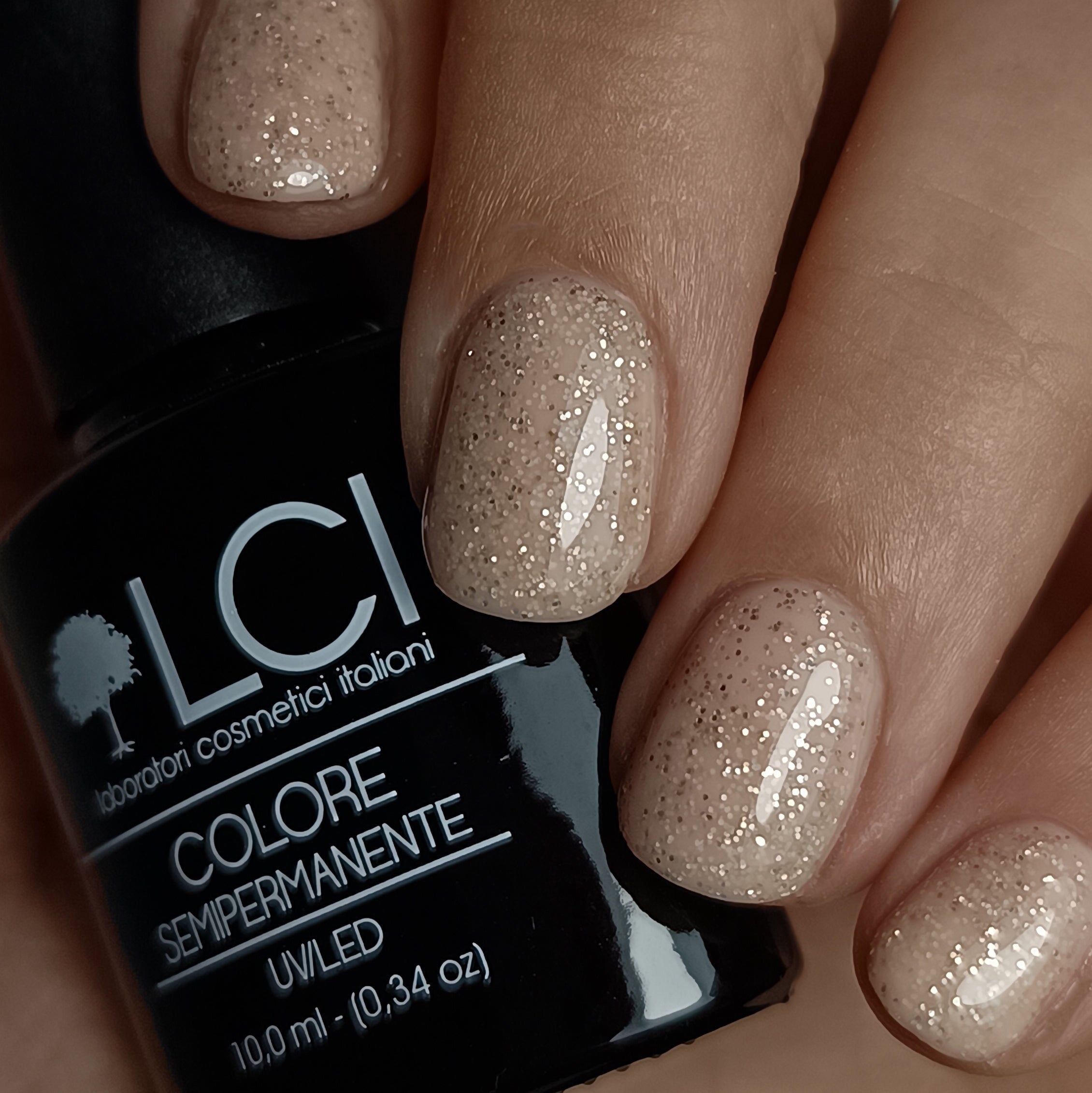 Mano con unghie smaltate. Unghie color sabbia con glitter. Flacone di smalto nero con etichetta sullo sfondo.