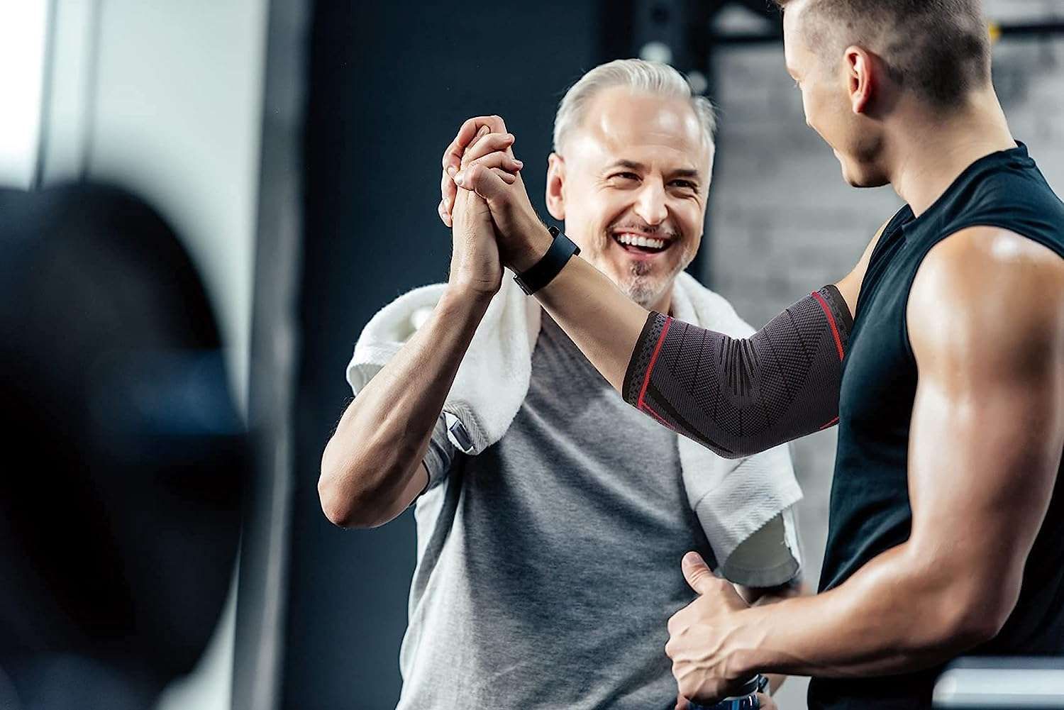 Uomo e donna si danno il cinque. L'uomo indossa un tutore per il gomito. Tutore grigio con dettagli rossi. In palestra.
