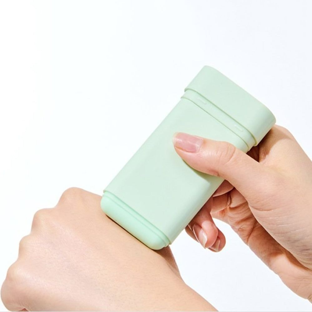 Una mano tiene uno stick solare verde chiaro. Lo stick viene applicato sulla pelle.