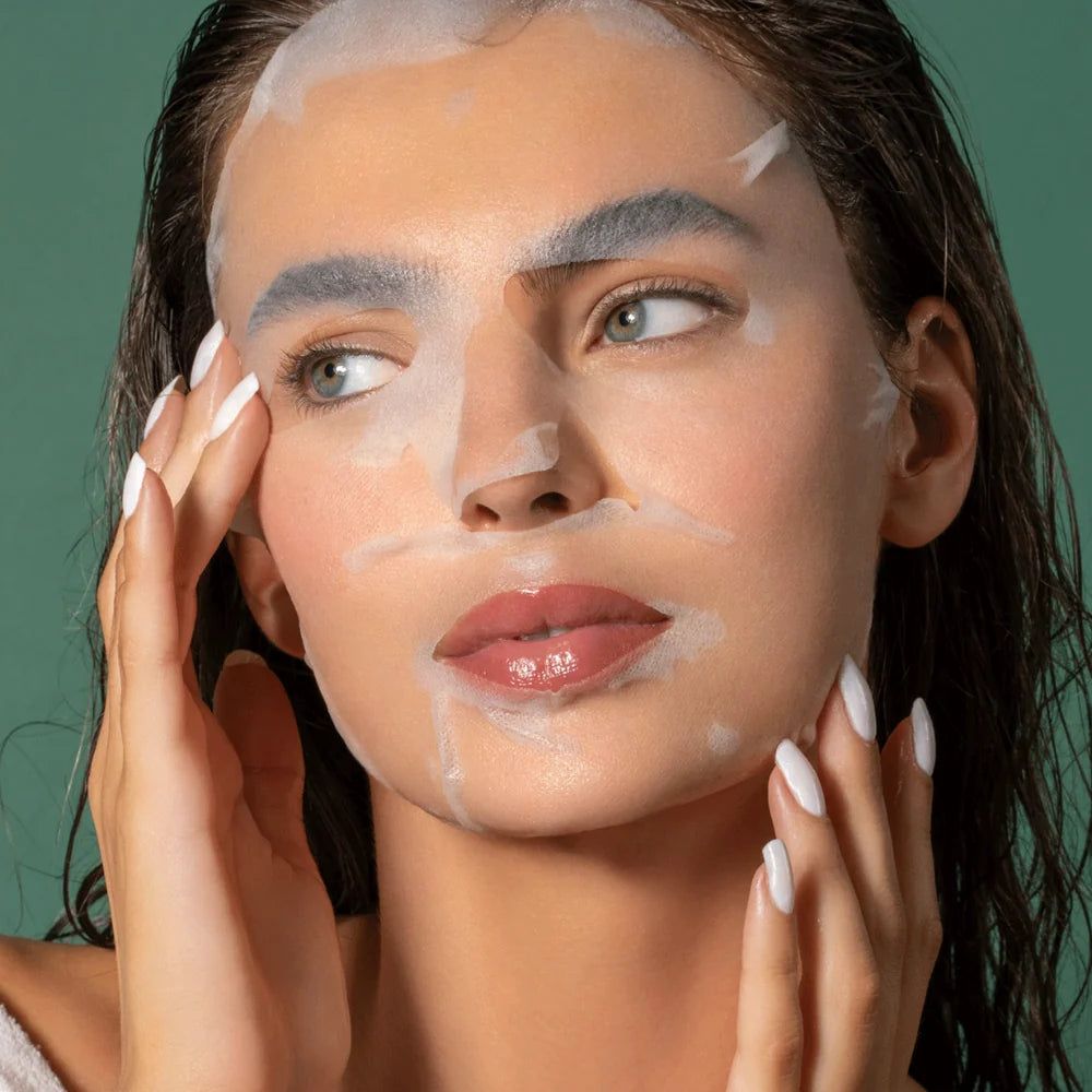 Donna con maschera per il viso. La maschera copre il viso, le mani toccano le guance. Sfondo verde.