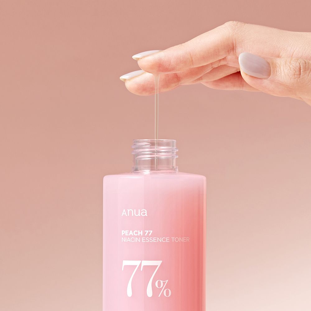 Una mano versa il tonico essenza niacinamide ANUA Peach 77% da una bottiglia.