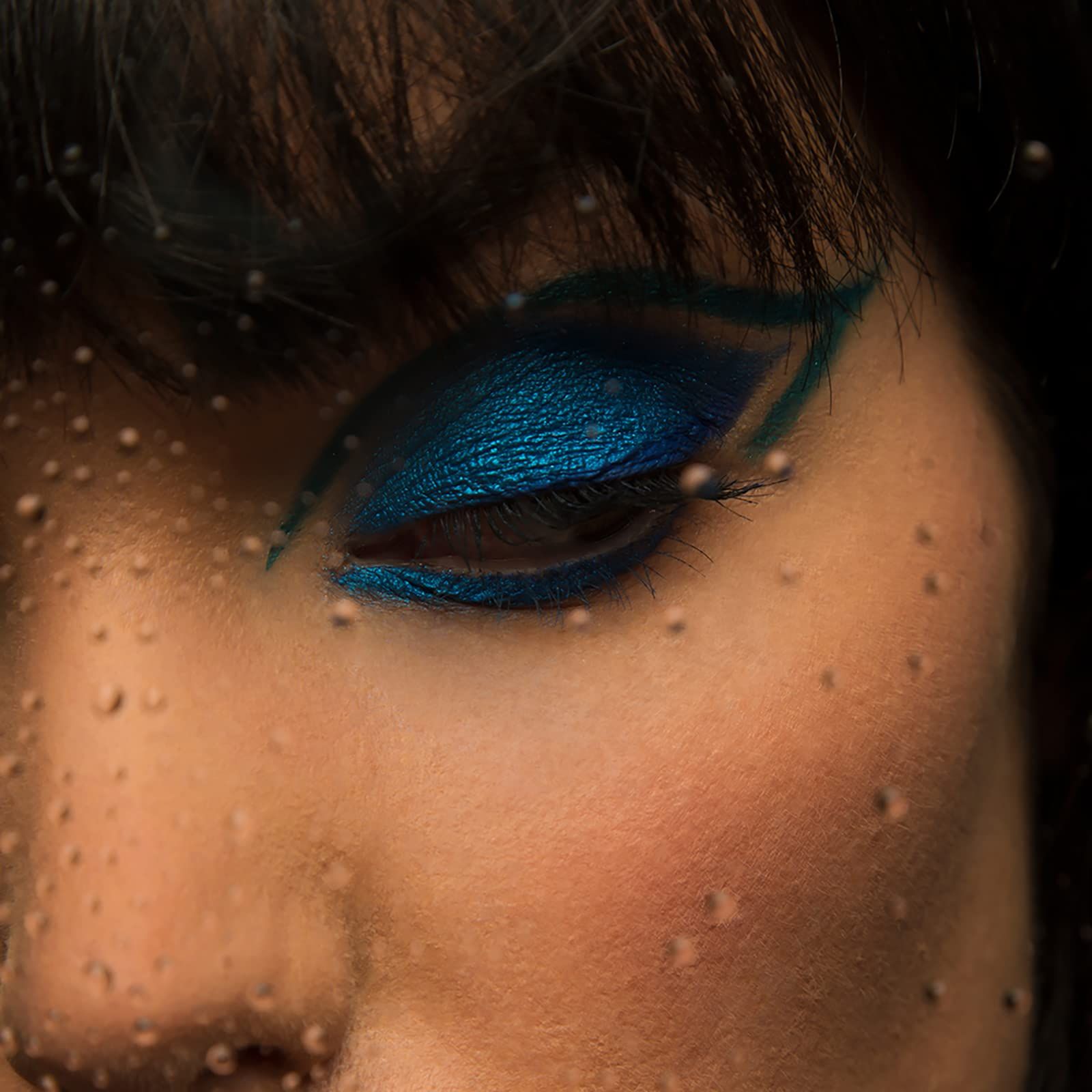 Occhio con ombretto blu. Gocce d'acqua sul vetro. L'ombretto è applicato sulla palpebra.