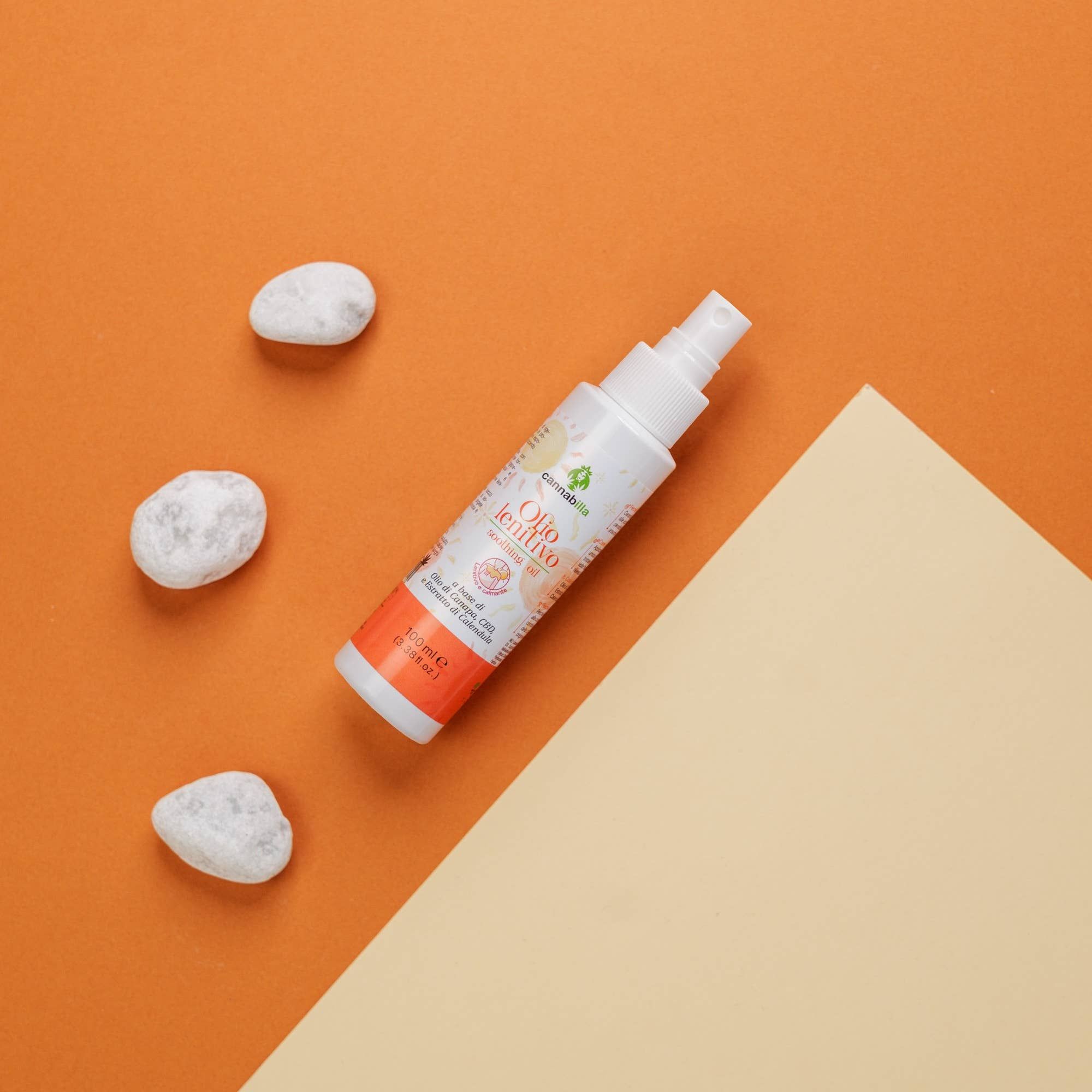 Flacone bianco con vaporizzatore su sfondo arancione. Accanto, tre pietre bianche e un triangolo beige.