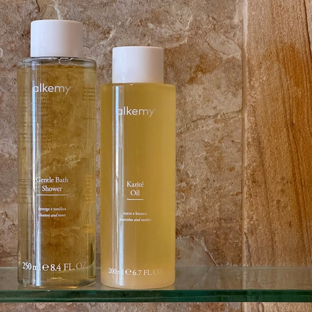 Due flaconi Alkemy: bagnoschiuma (250ml) e olio di karité (200ml) su uno scaffale.