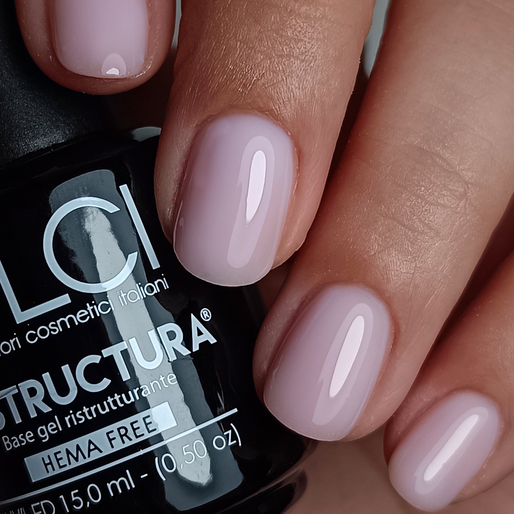 Mano con unghie smaltate. Colore: lilla chiaro. Scritta: Restructura Base gel ristrutturante HEMA FREE.