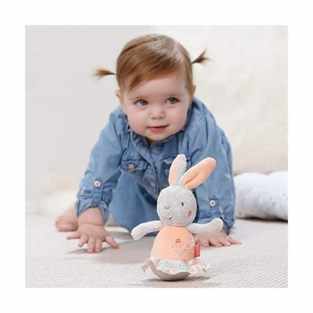 Bambino che gattona verso un coniglietto di peluche grigio, pancia e orecchie rosa. Marchio: Fehn.