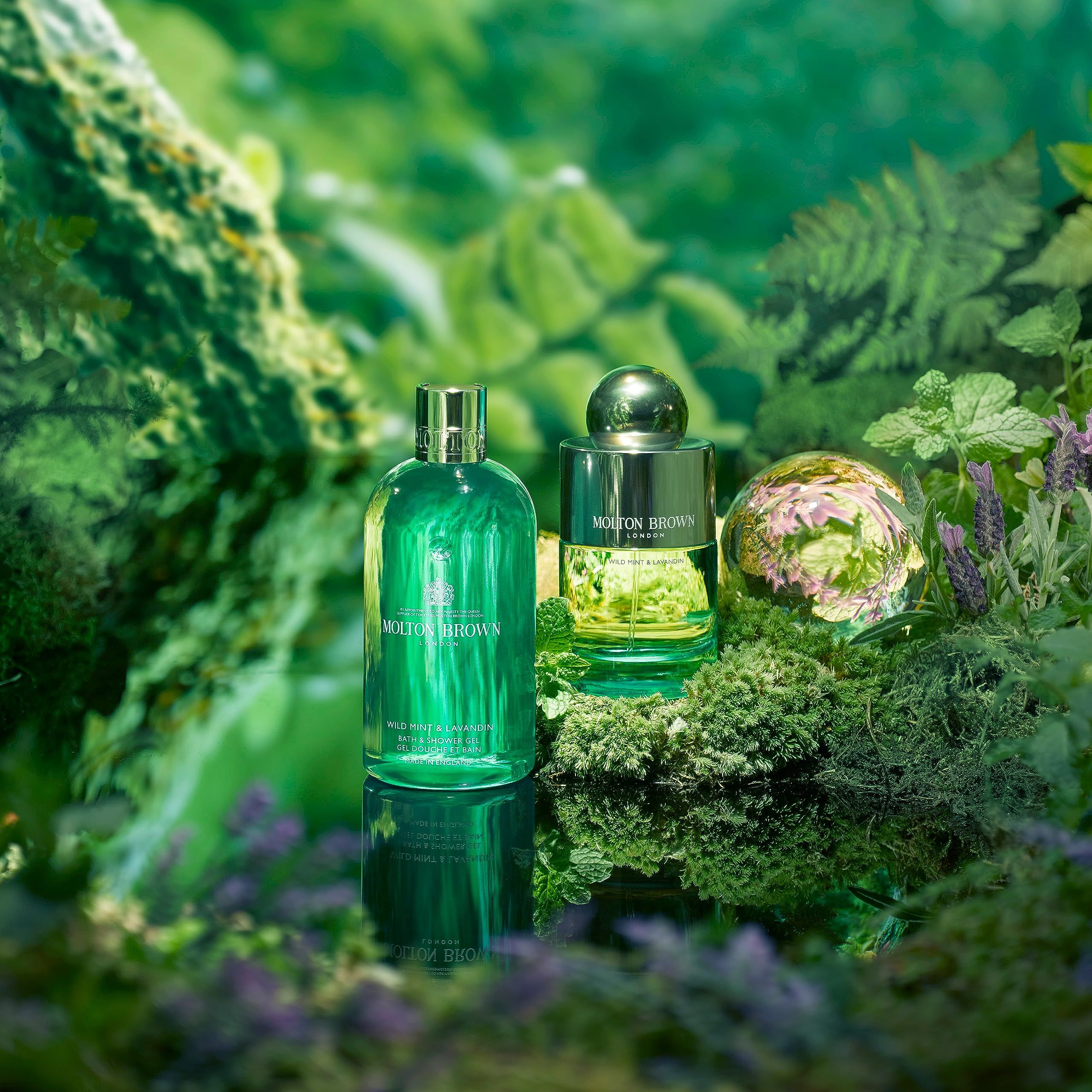 Due flaconi di profumo su una superficie verde riflettente, circondati da piante e fiori.