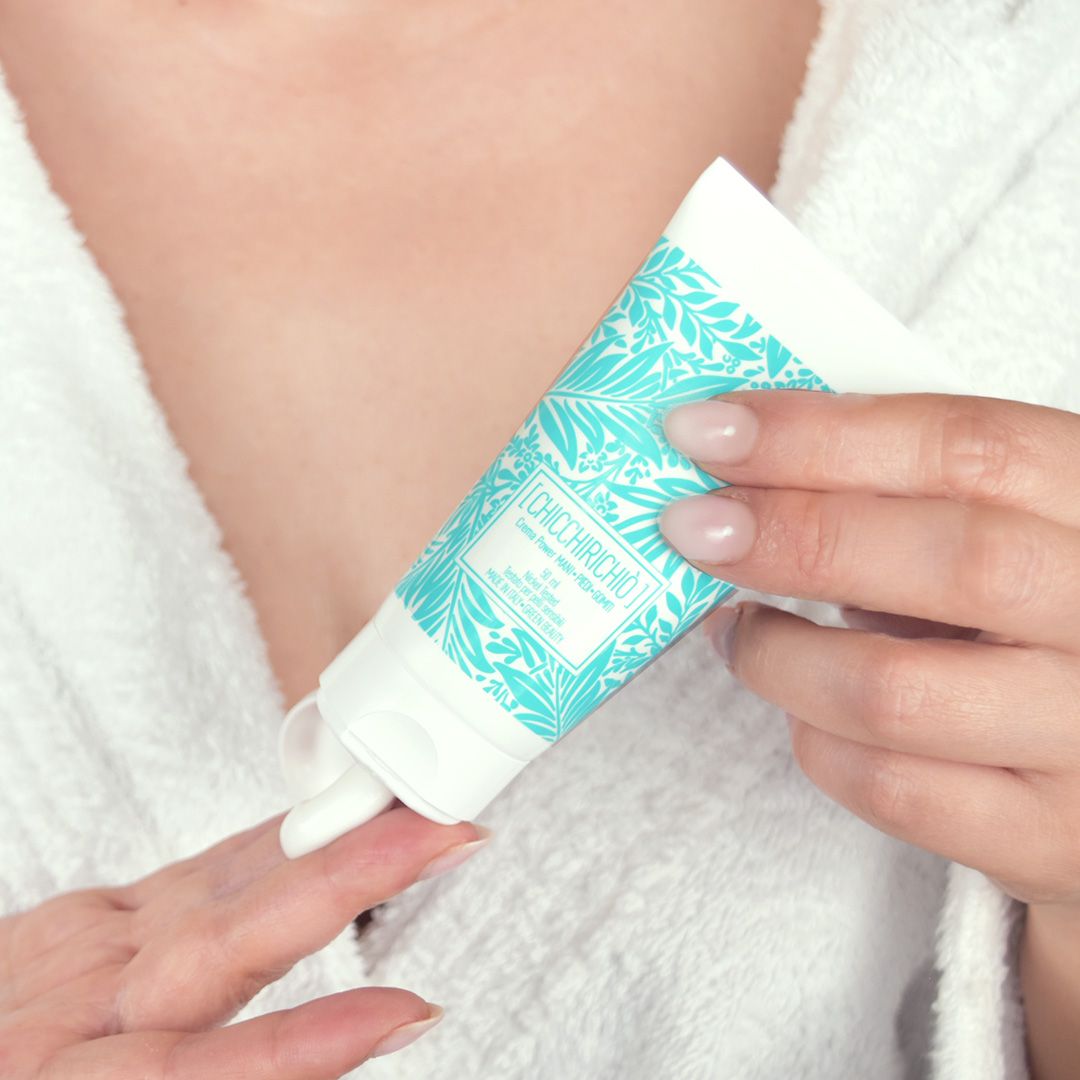 Applicazione di crema su un dito. Tubo bianco con motivo turchese e testo. Scritta: Chicchirichiò Crema Mani.