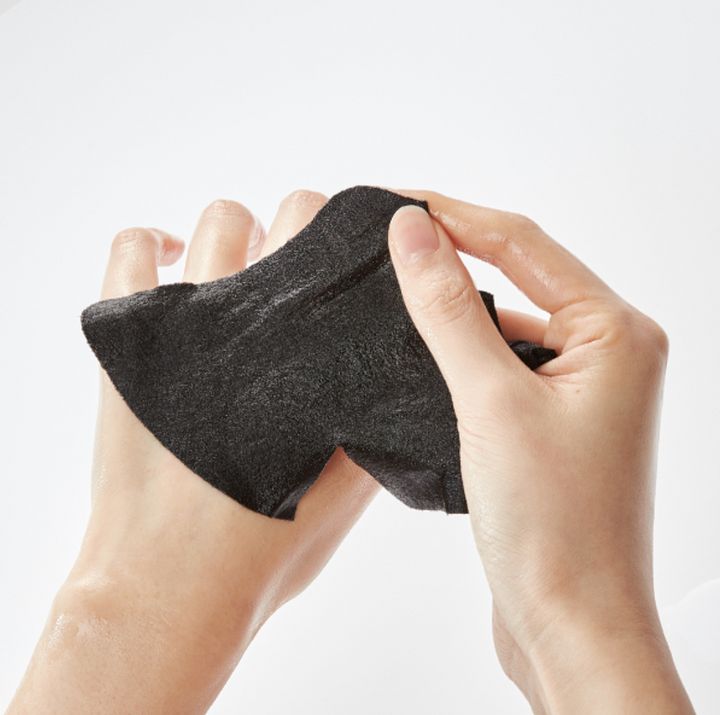 Mani che tengono una maschera per il viso nera. La maschera è fatta di materiale nero e leggermente umido.