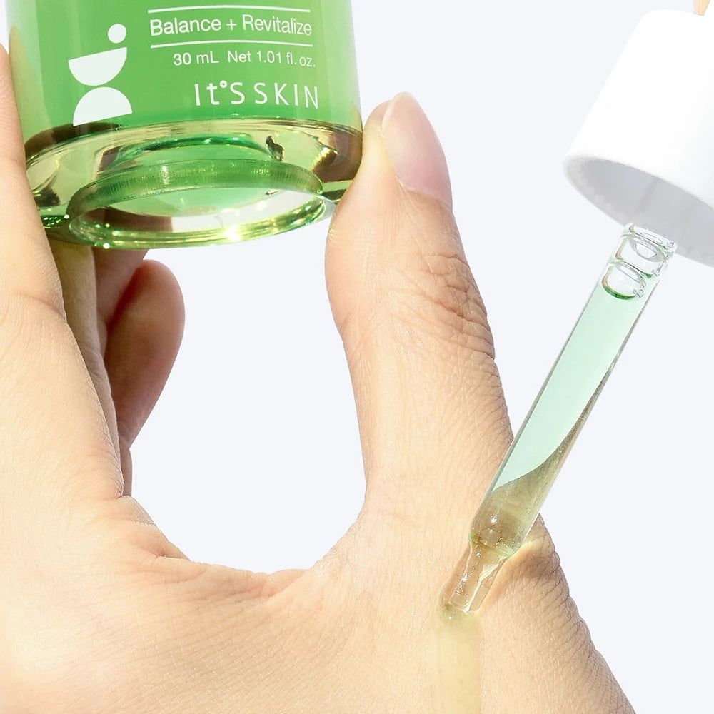 Mano che tiene flacone e pipetta. Pipetta che preleva liquido verde. Nome prodotto: IT'S SKIN.