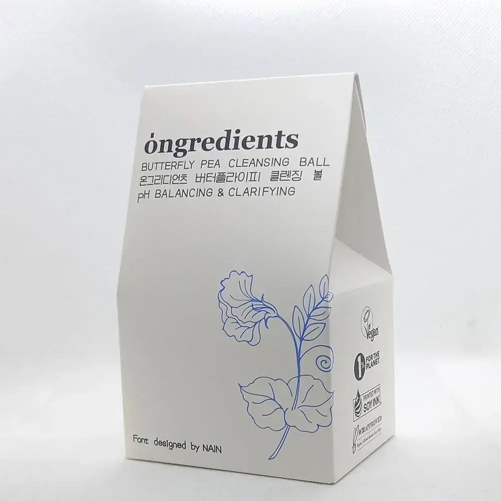 Confezione bianca con motivo floreale blu e testo. Contiene loghi Vegan, 0% for the planet e inchiostro di soia.