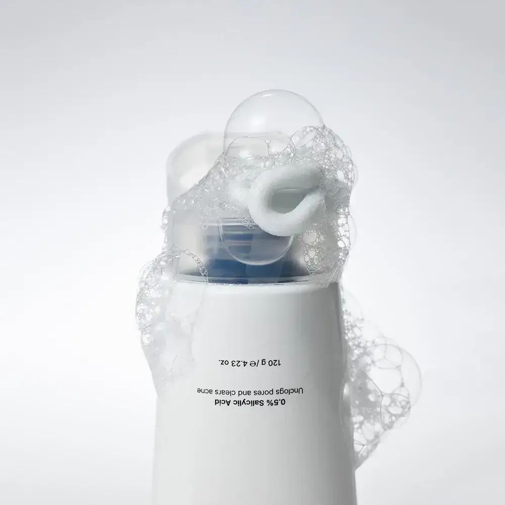 Flacone bianco con schiuma. Scritta: 0,5% acido salicilico. Rimuove le impurità e schiarisce l'acne. 120 g / 4,23 oz.