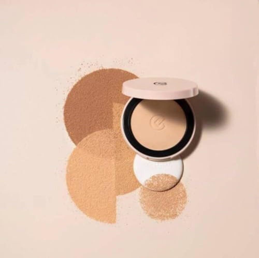 Cipria compatta con nuvole di polvere e applicatore. Confezione rosa chiaro aperta. Anello nero attorno alla cipria. Logo in rilievo.