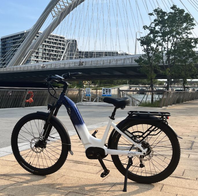 E-bike bianca e blu con motore centrale. Ponte sullo sfondo. Pneumatici neri, portapacchi, sella.