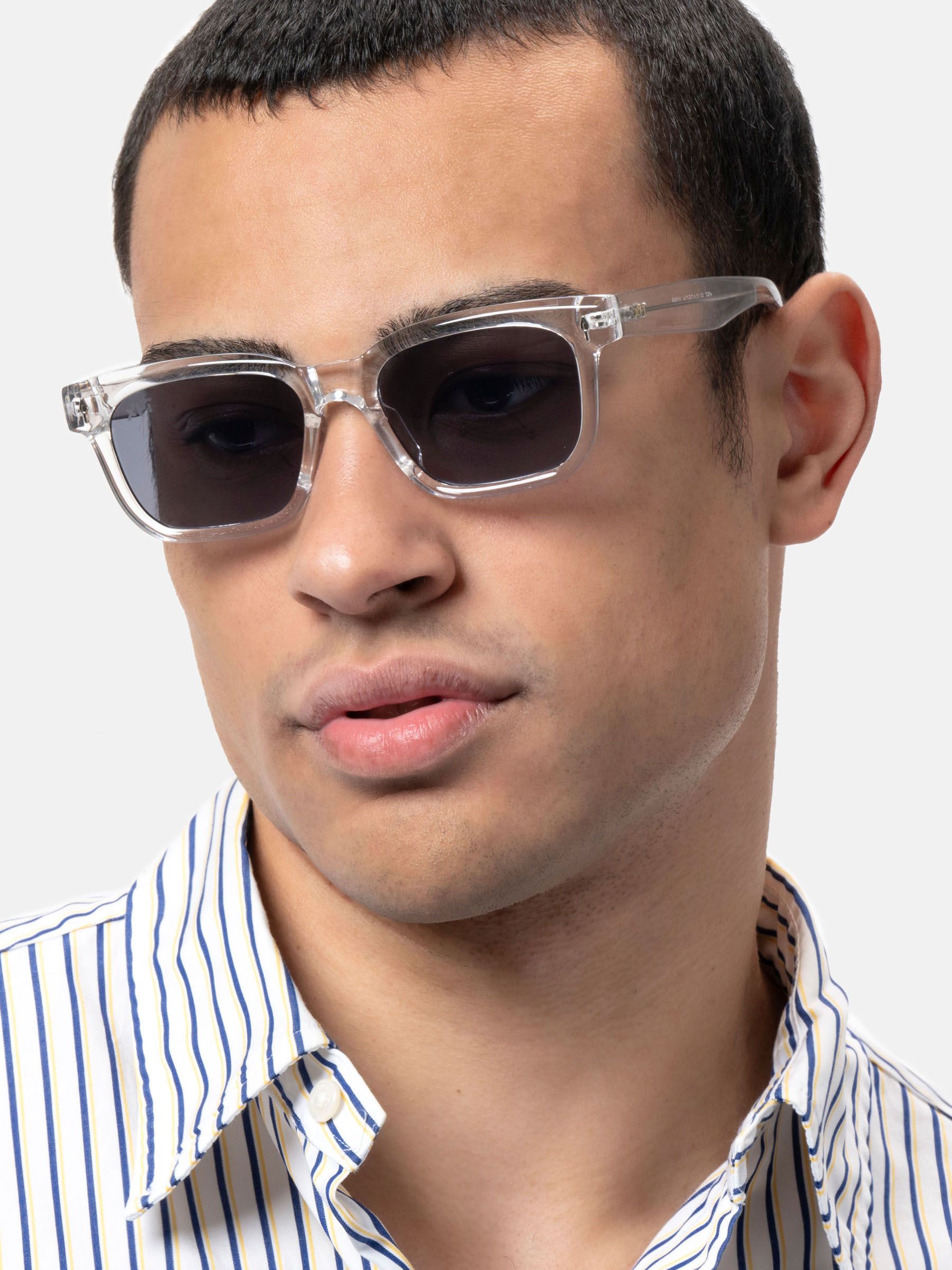 Uomo con occhiali da sole trasparenti, lenti scure. Forma rettangolare, logo XFT sull'asta.