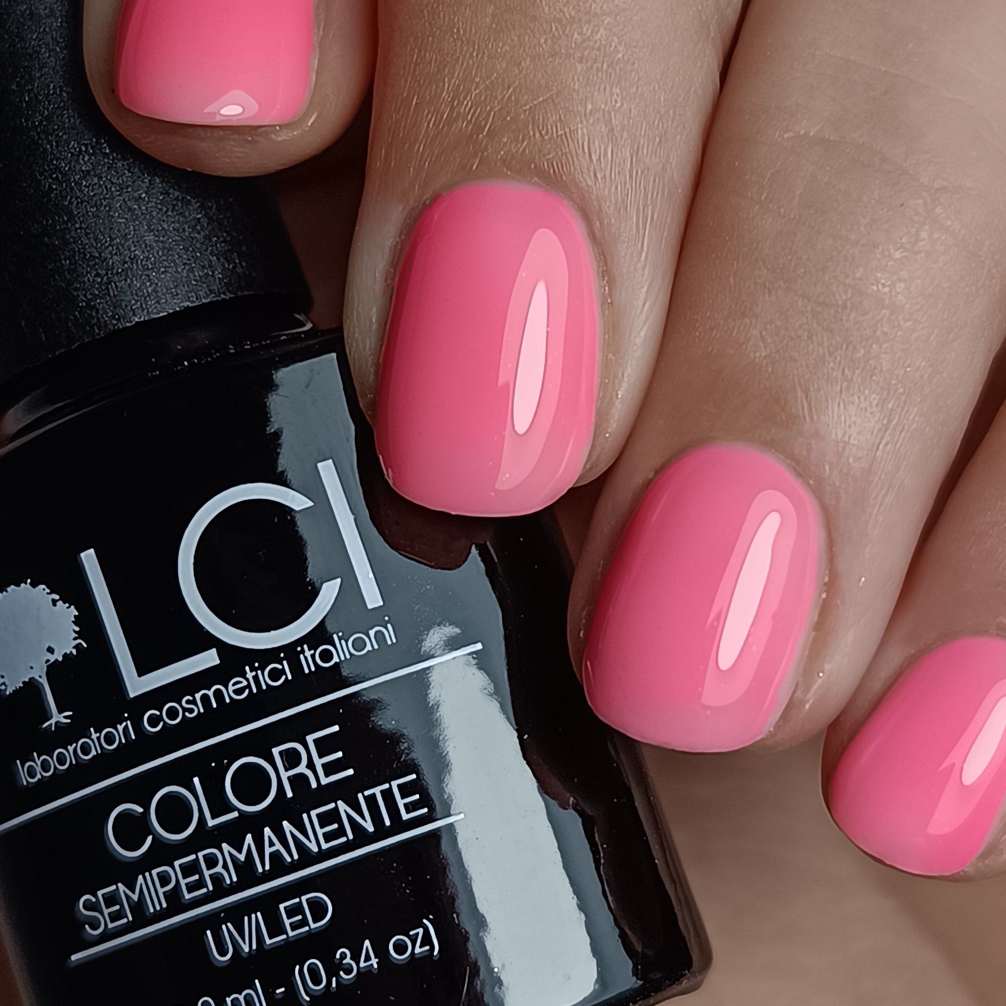 Primo piano di unghie smaltate di rosa. Flacone con tappo nero e scritta: LCI, Colore Semipermanente.