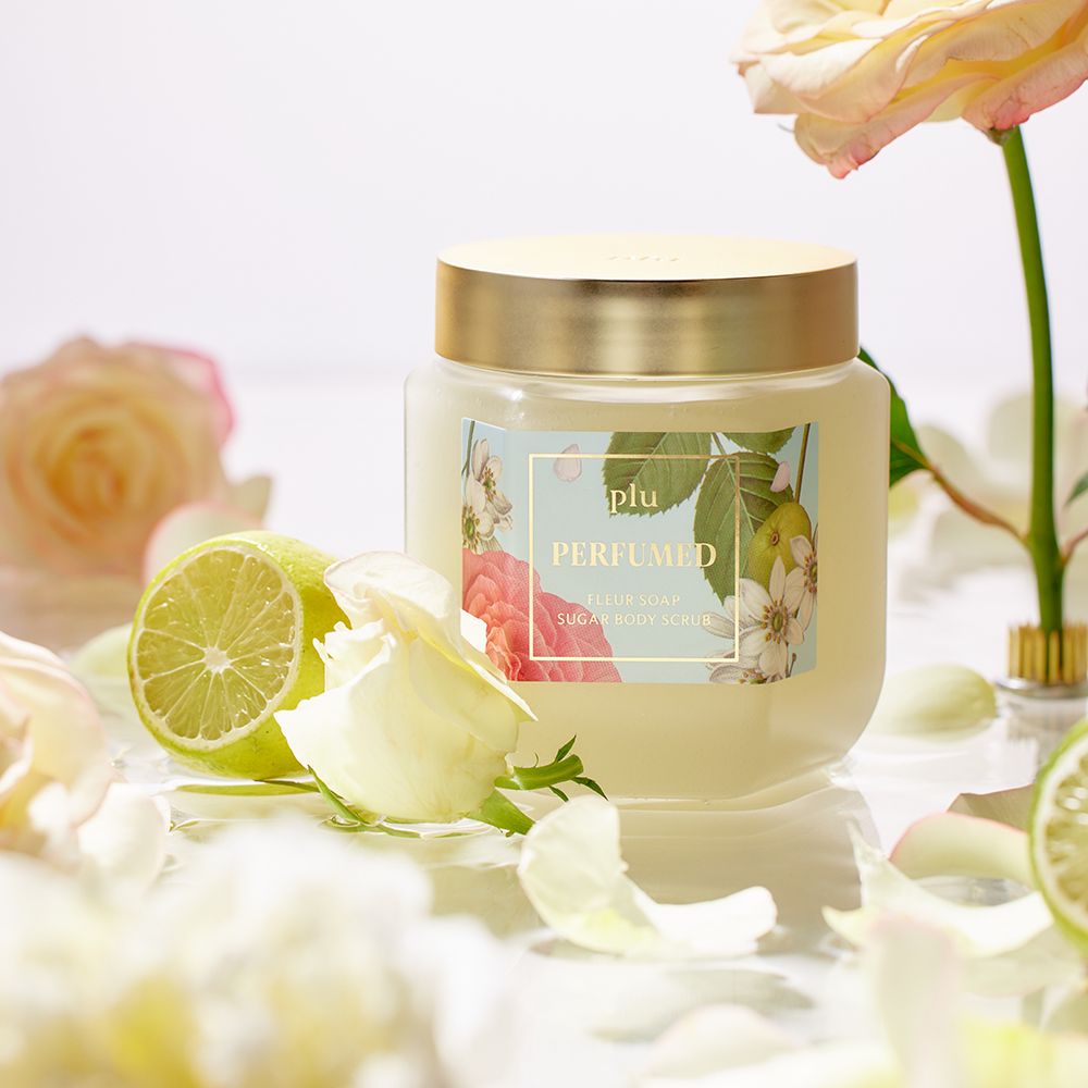 Vaso con coperchio dorato, etichetta floreale. Fette di lime e petali circondano il prodotto.