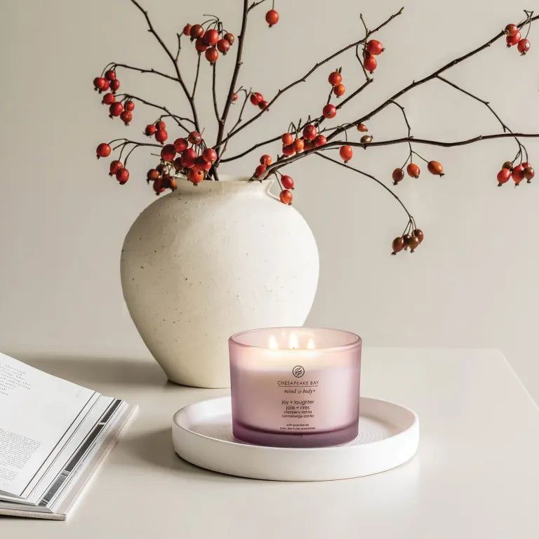 Candela rosa a tre stoppini su un vassoio bianco. Sullo sfondo, un vaso con rami e bacche rosse. Scritta: Chesapeake Bay.