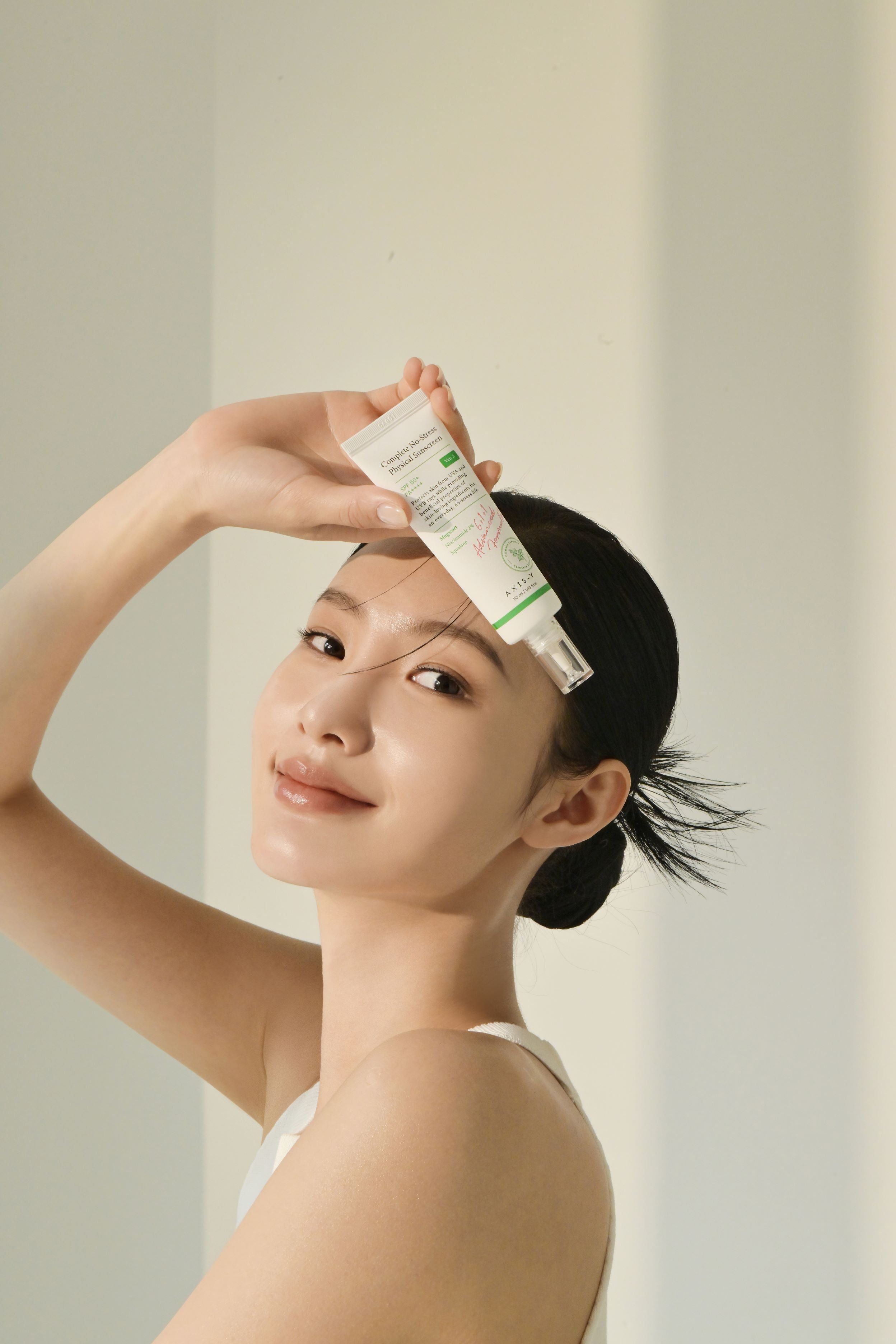 Donna tiene un tubetto di AXIS-Y Complete No-Stress Physical V.3 SPF 50. Prodotto sulla fronte.