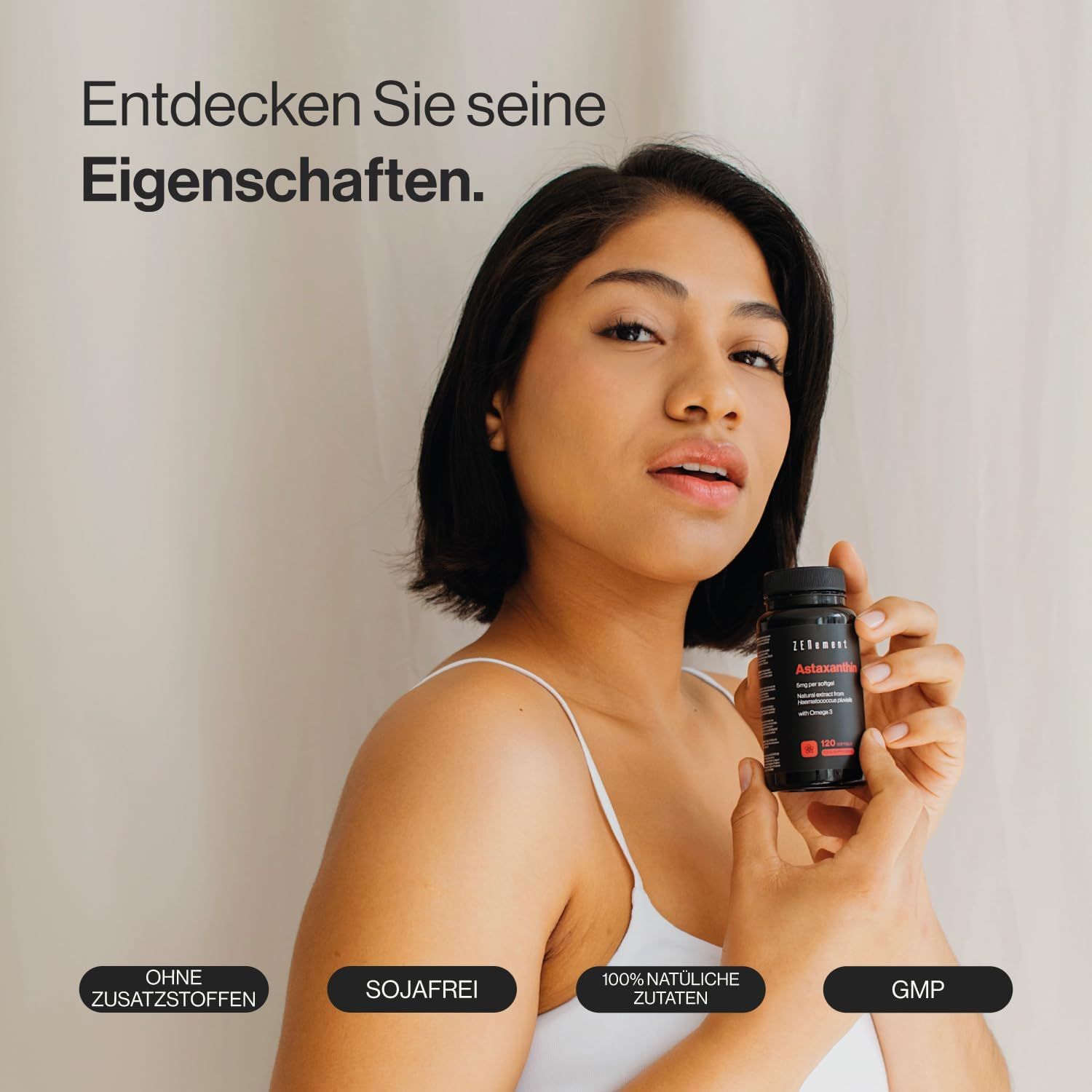 Donna tiene in mano una bottiglia nera con etichetta rossa. Sulla bottiglia c'è scritto Astaxantina. Scritte: Senza additivi, Senza soia, 100% ingredienti naturali, GMP.