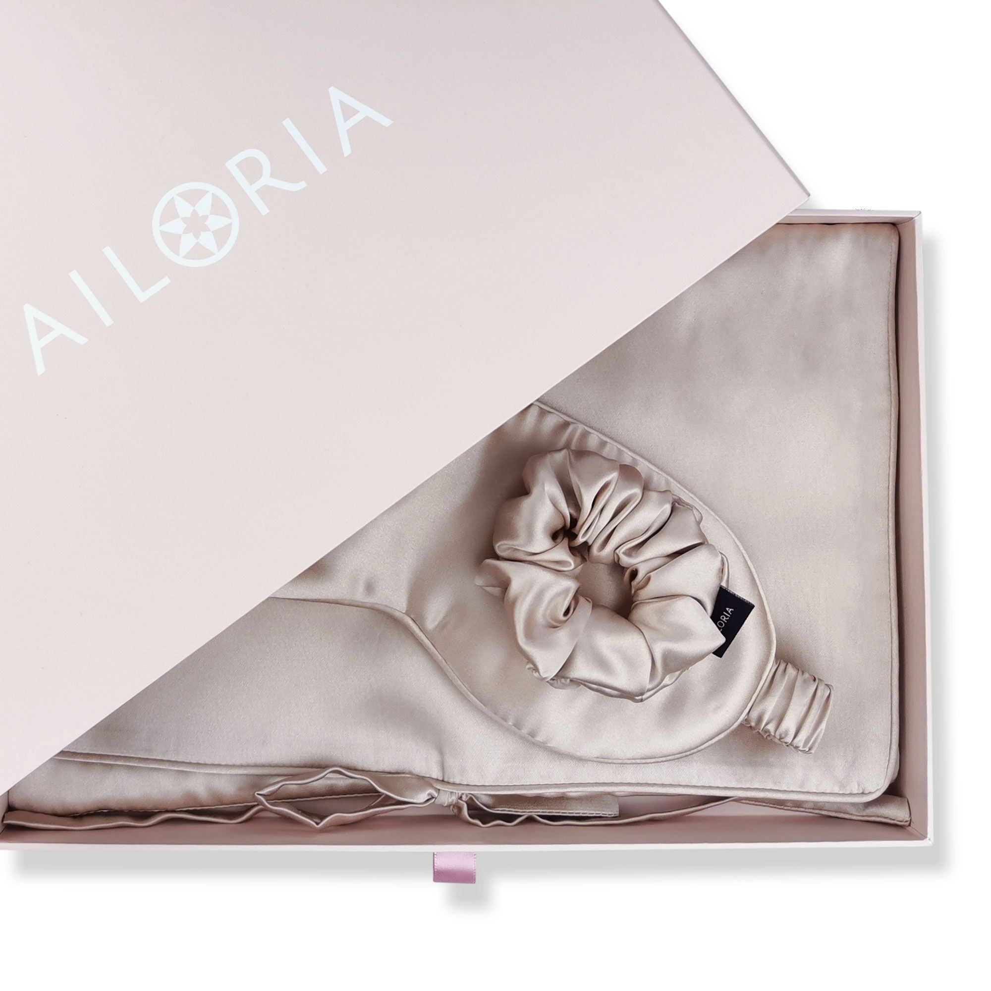 Maschera per dormire e scrunchie in seta in una scatola rosa con logo 'AILORIA'.