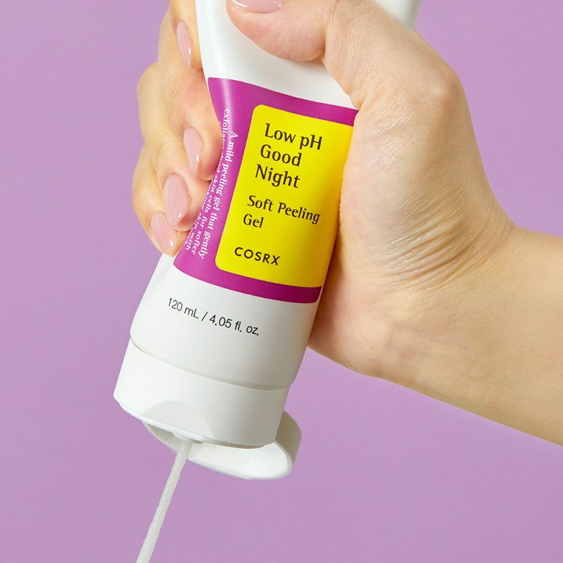 Mano che preme un tubo bianco. Scritta: Low pH Good Night Soft Peeling Gel. Marchio COSRX. Gel che esce. Sfondo viola.