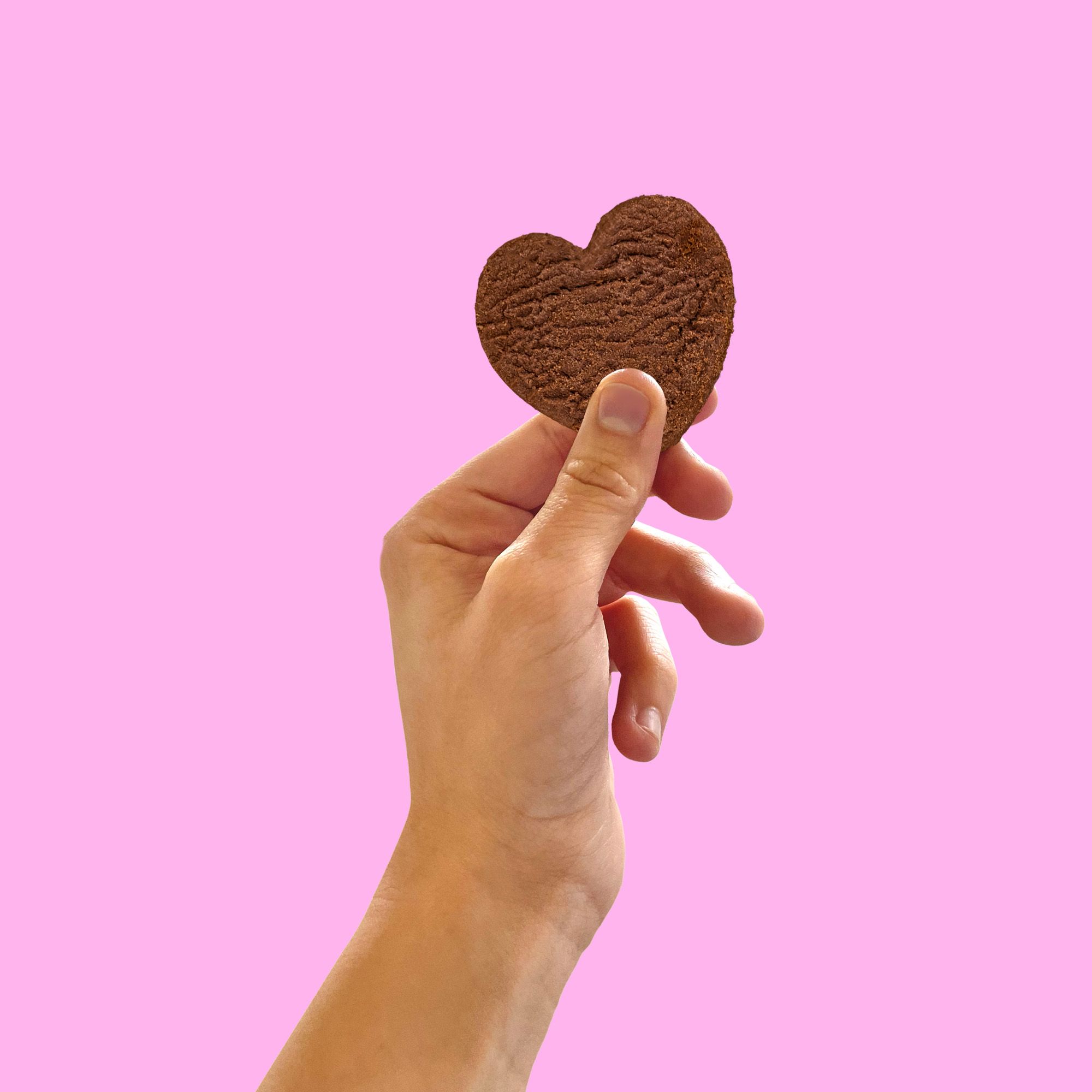 Mano che tiene un biscotto IoBoscoVivo senza glutine a forma di cuore su sfondo rosa.