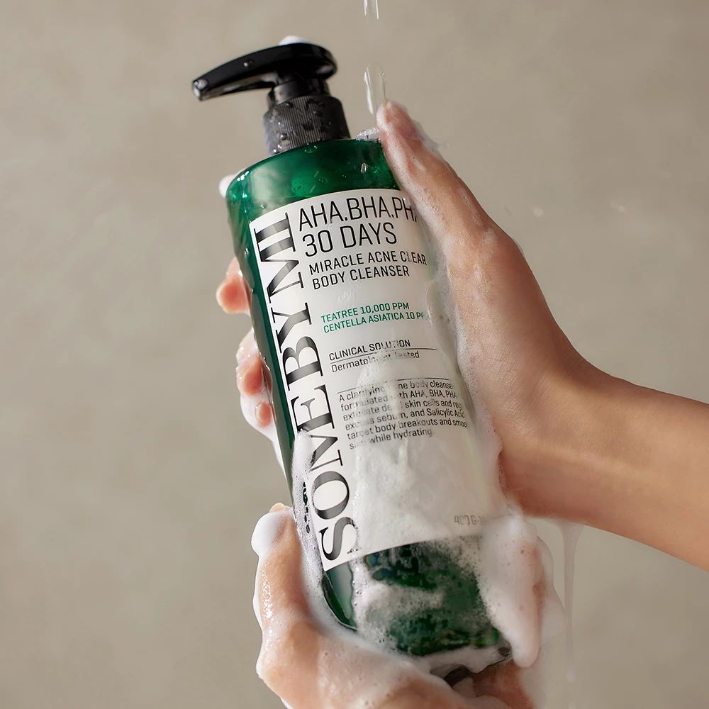 Mani che tengono un flacone del detergente corpo SOMEBYMI AHA BHA PHA 30 giorni Miracle Acne Clear sotto l'acqua.