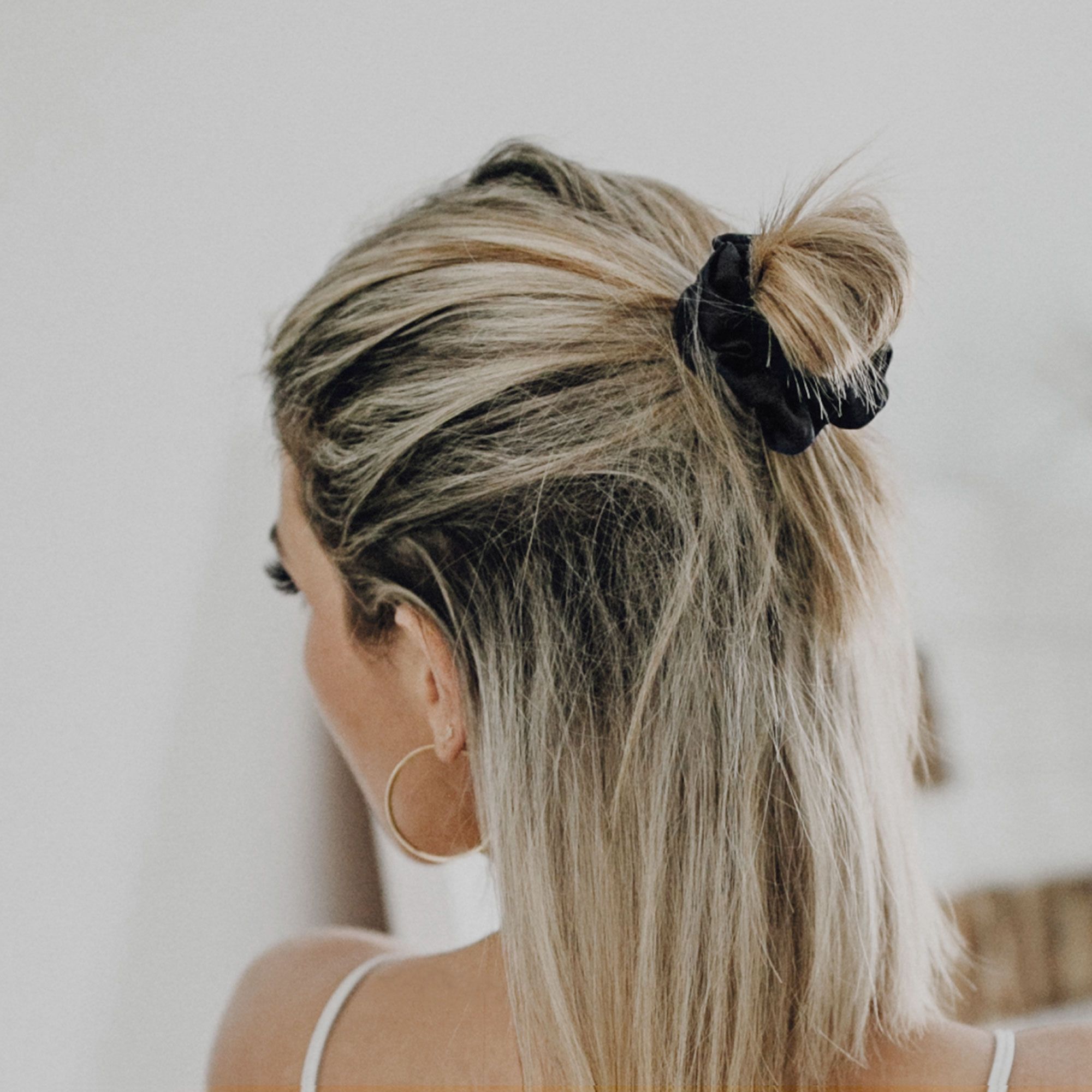 Donna con capelli biondi, indossa uno scrunchie in seta nero nei capelli.