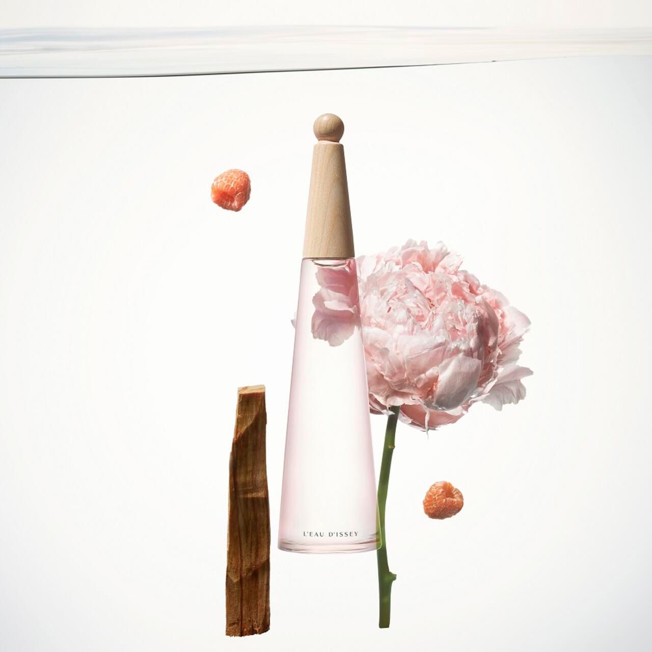 Flacone rosa, tappo in legno, peonia, legno, pezzi di frutta. L'Eau d'Issey.